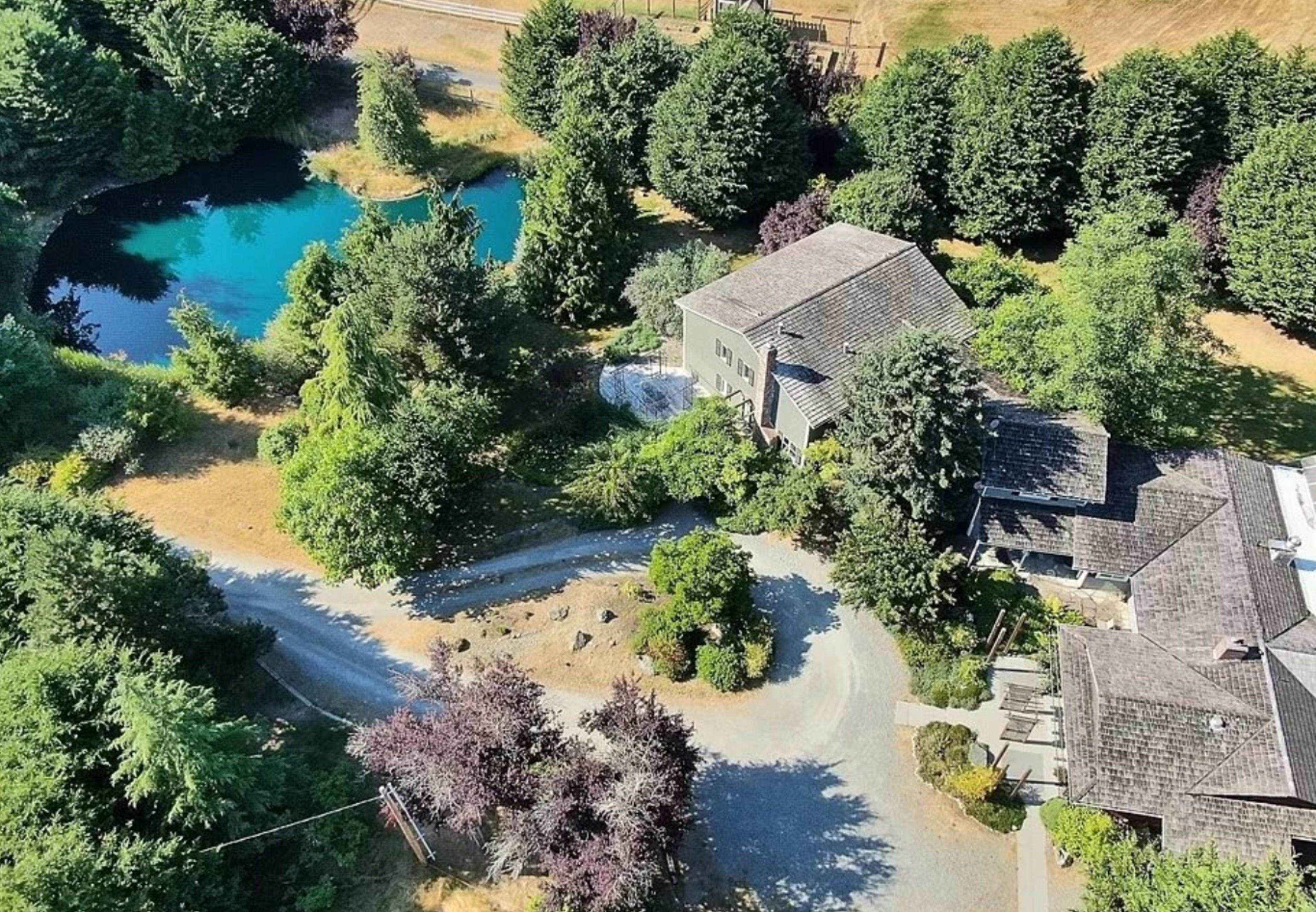 An aerial view shows a house surrounded by trees and a blue pond, with a winding driveway leading to the entrance.
