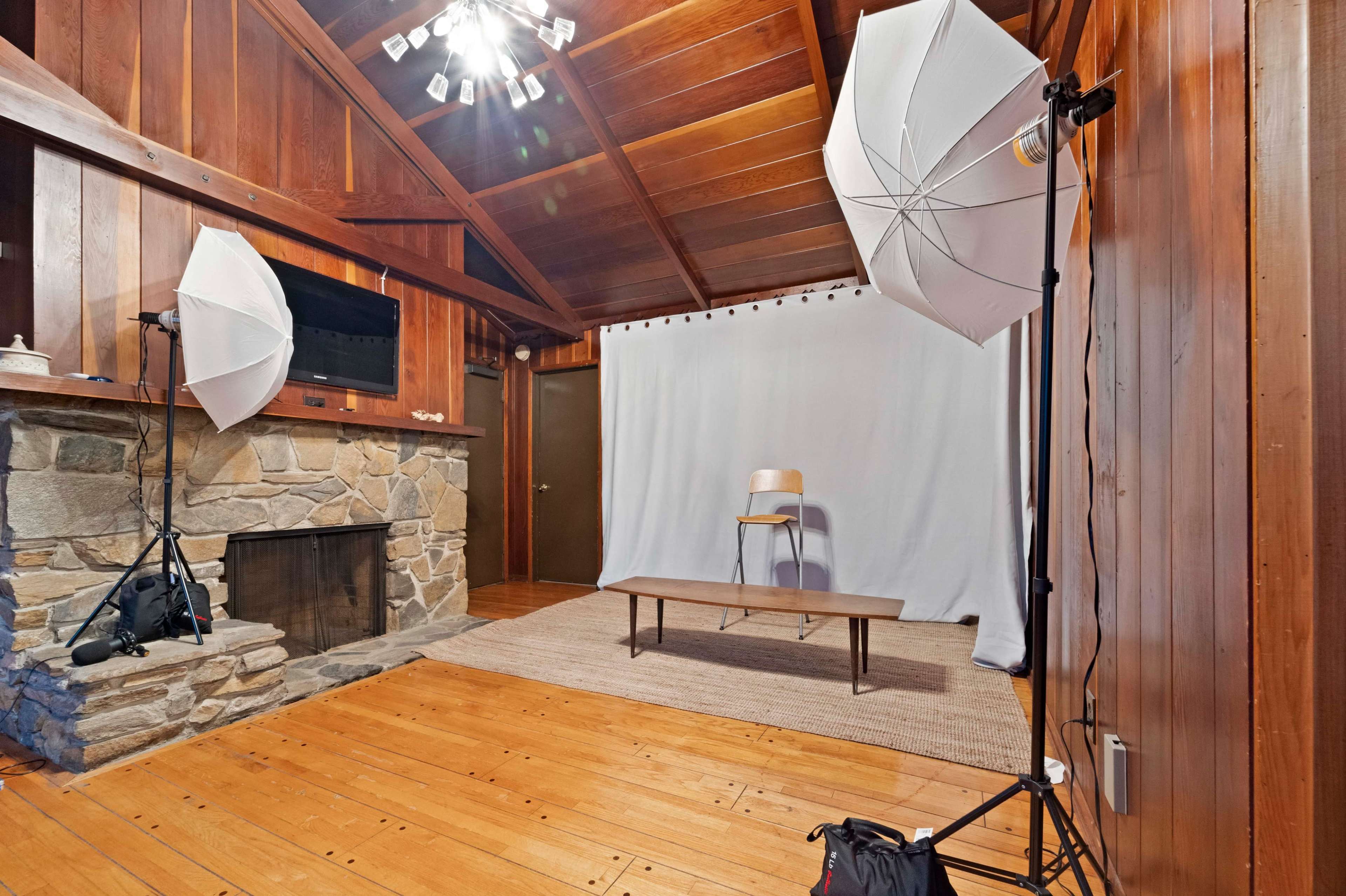 A room with wooden walls, a stone fireplace, a plain white backdrop with a wooden bench, and two softbox lights positioned on either side.