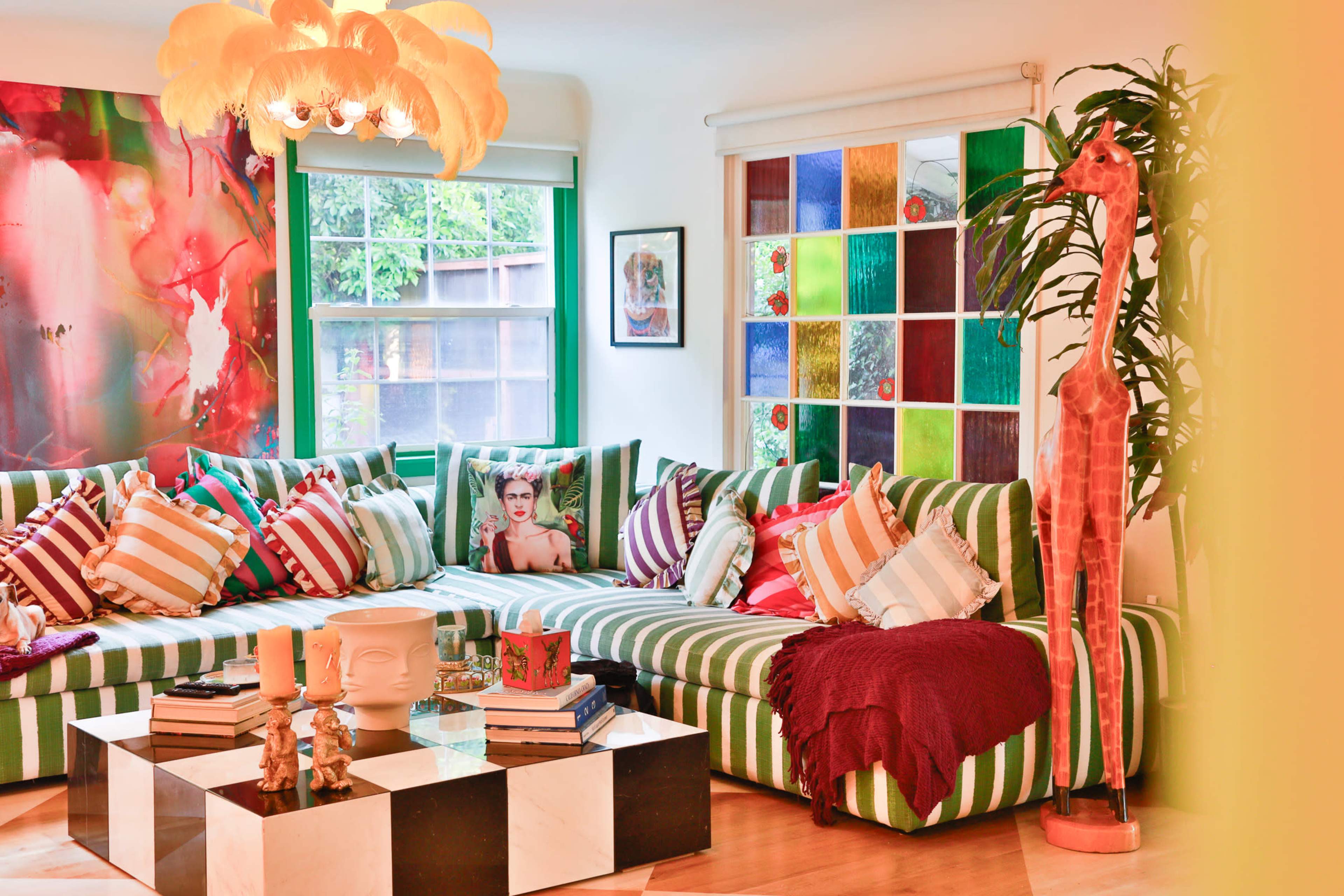 The living room features a large striped sofa adorned with colorful pillows, a coffee table with stacked books, and vibrant artwork on the walls.