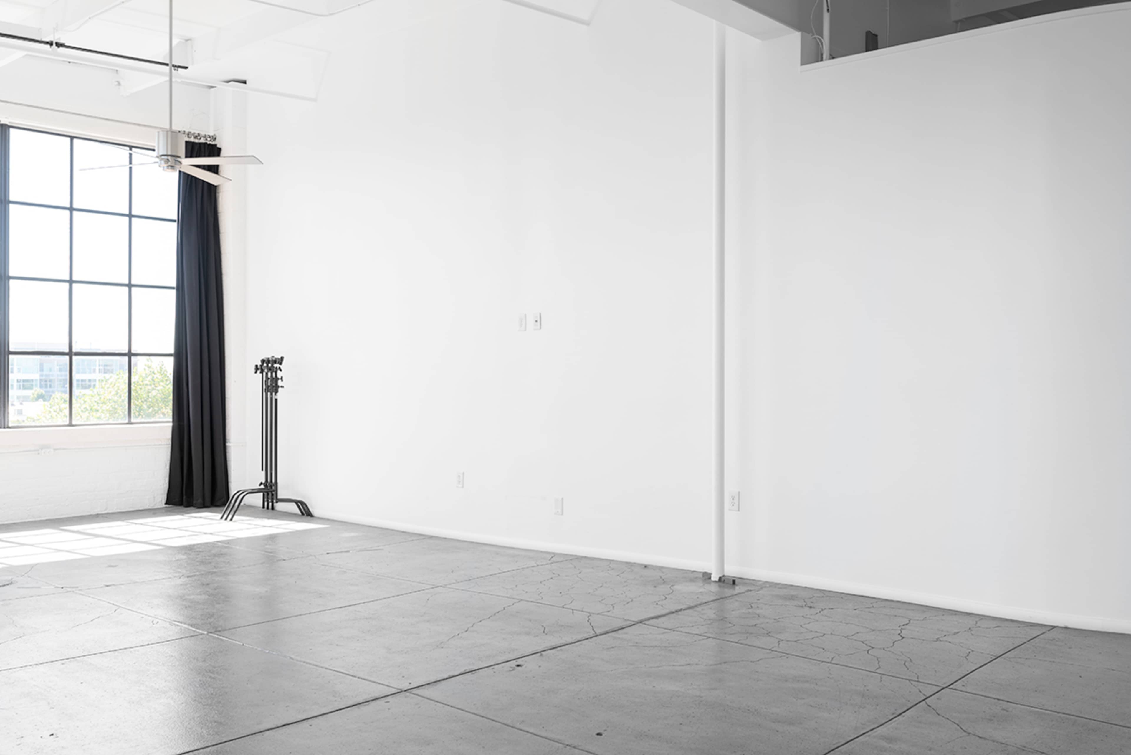 An empty room with a large window, a black curtain, and exposed concrete flooring.