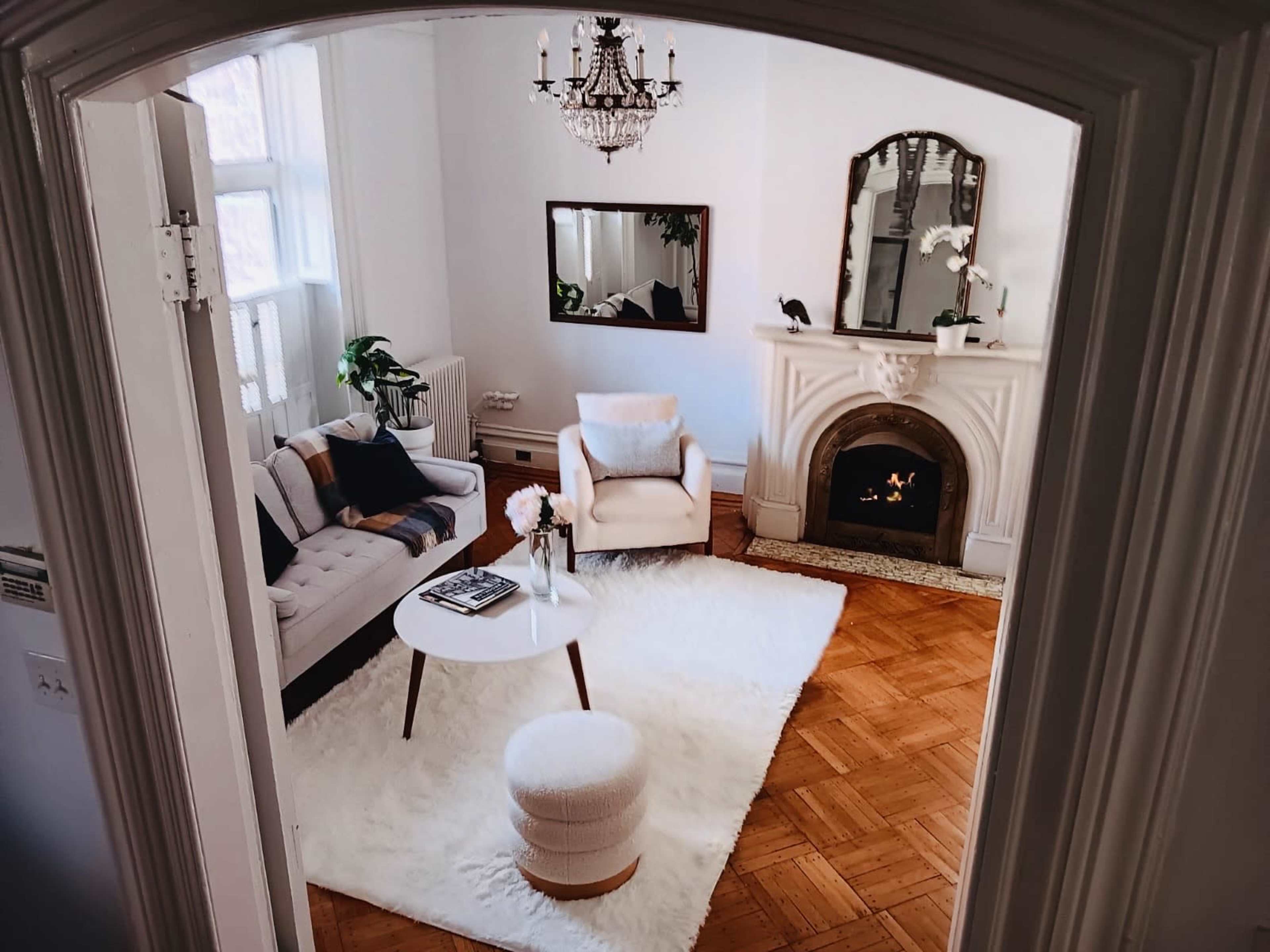 A bright living room featuring a light-colored sofa, a small round table, a plush rug, and a decorative fireplace.