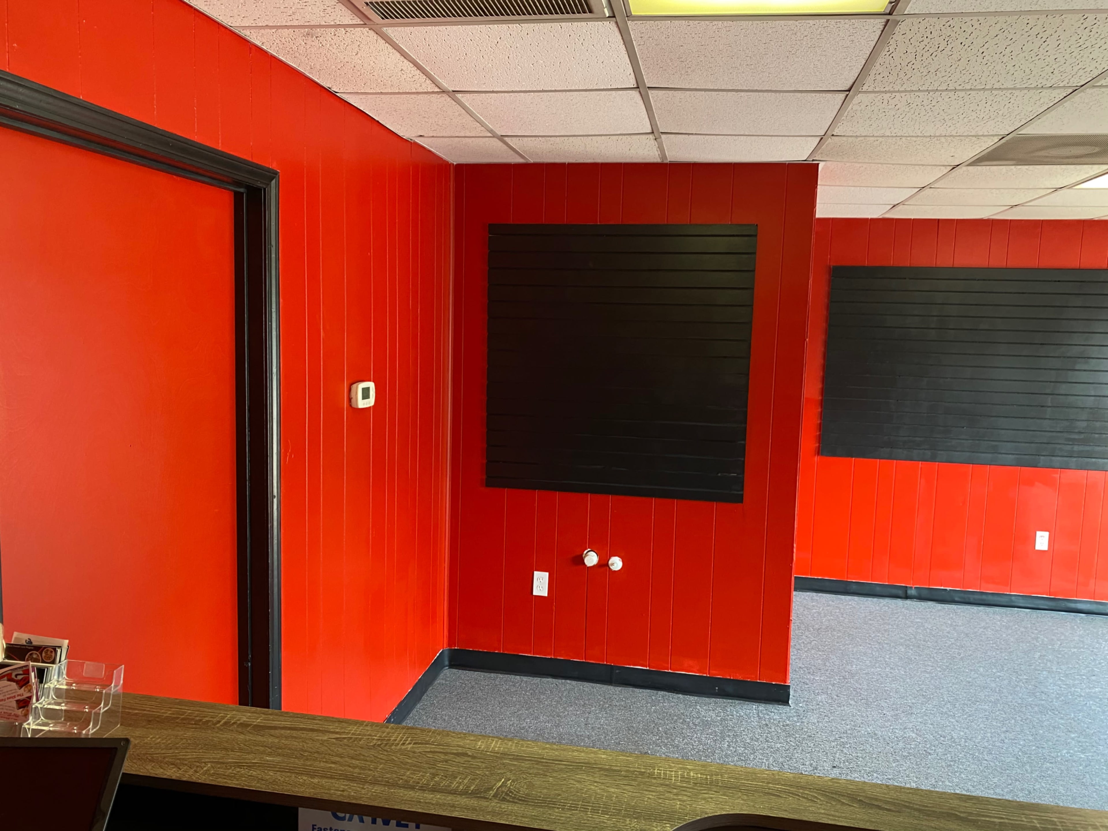 A room with bright red walls, a dark black wall panel, and a gray carpeted floor.