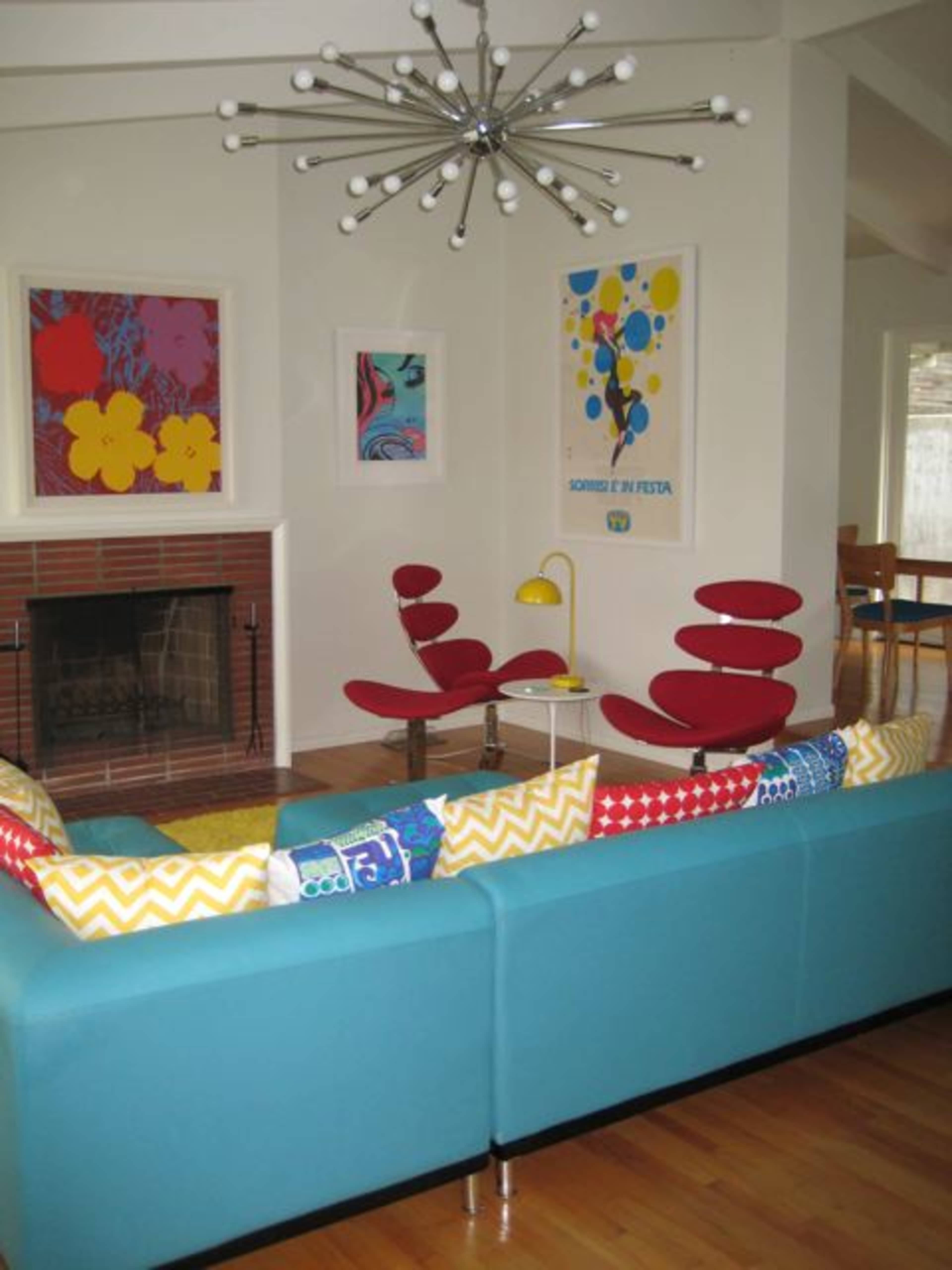 The living room features a blue sofa, red chairs, a modern light fixture, and colorful artworks on the walls.