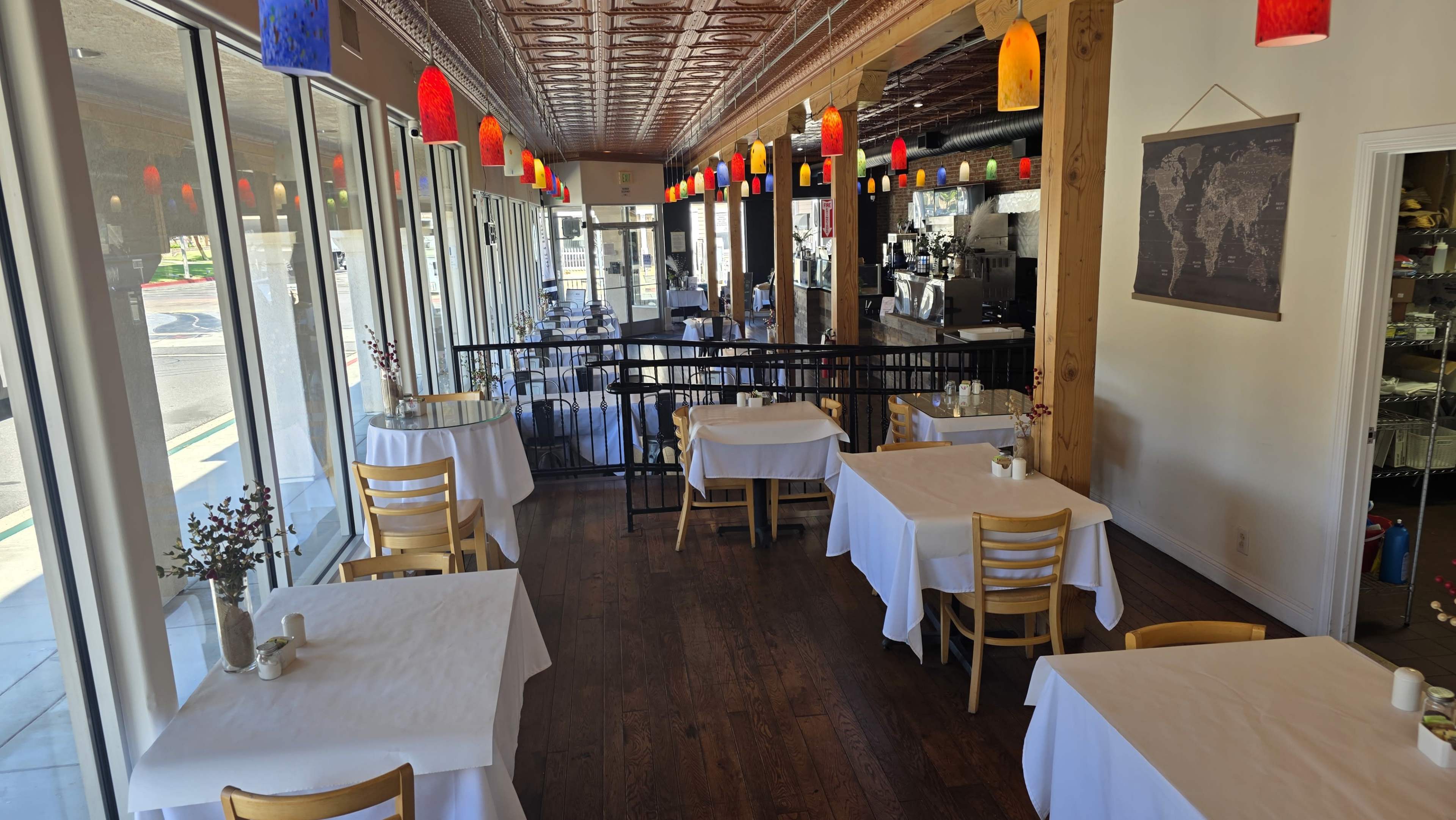 The image shows a spacious restaurant interior featuring several white-covered tables with wooden chairs, illuminated by colorful hanging lights.