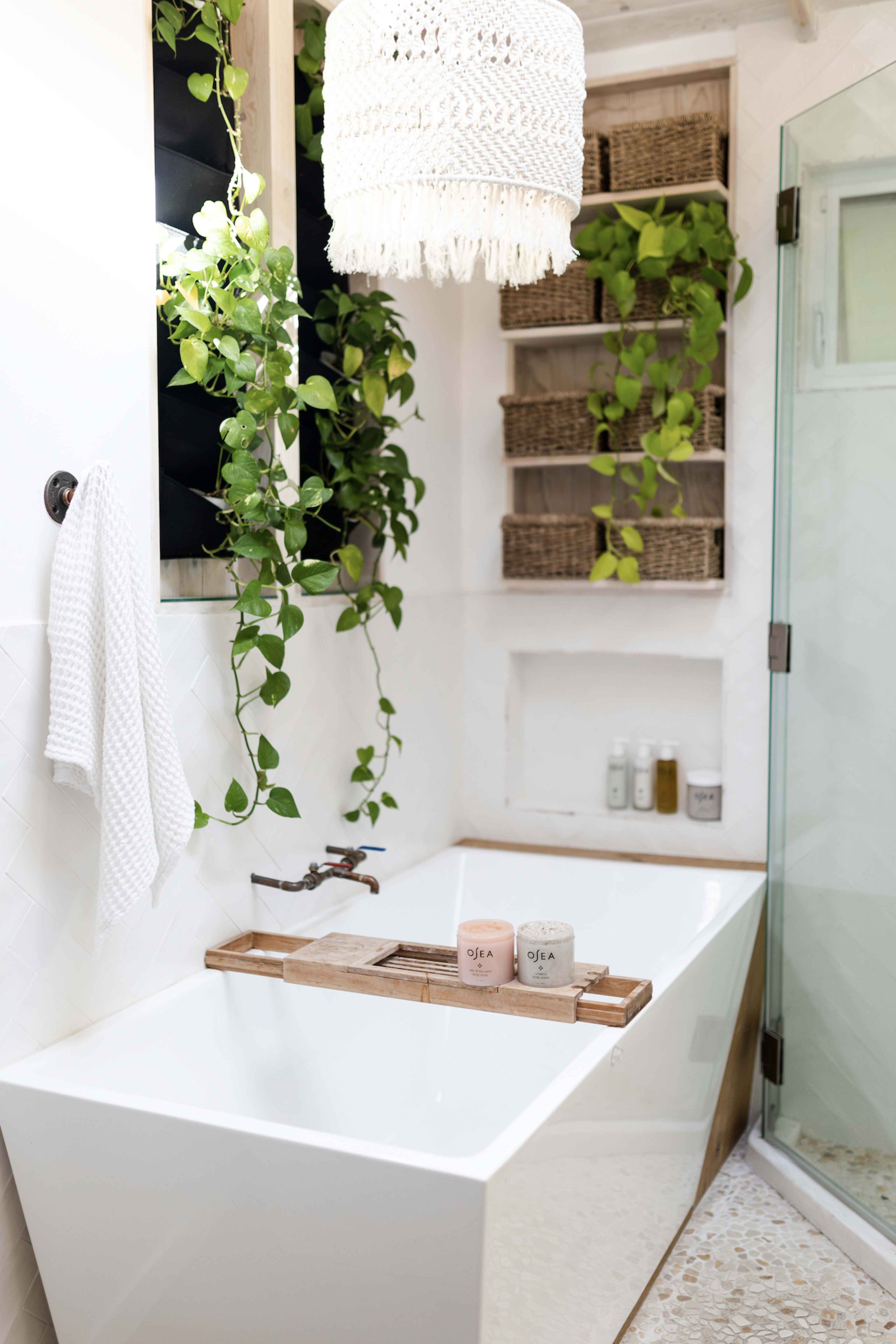 A photoshoot of a white bathtub and shower surrounded by plants.