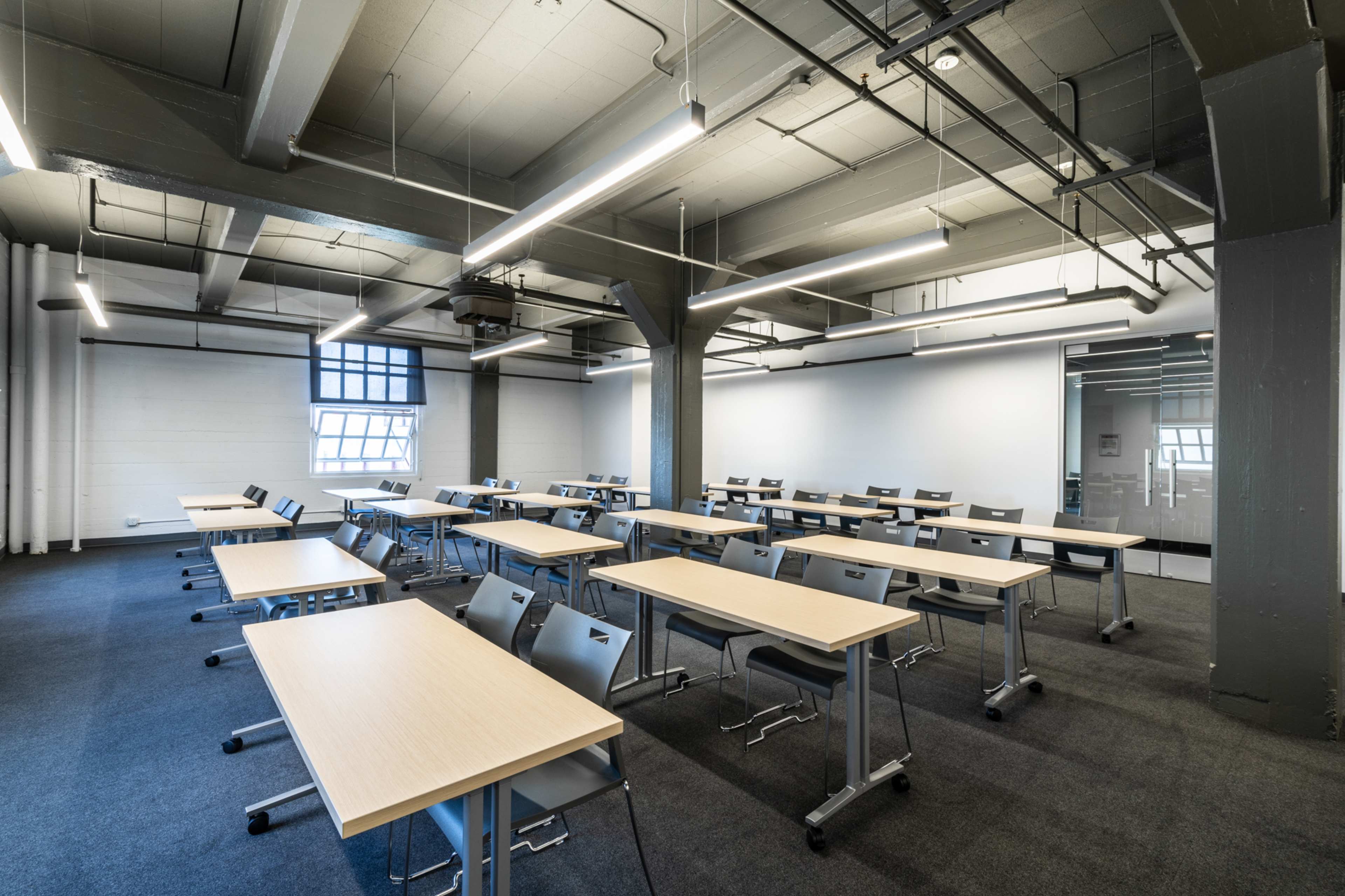 A modern classroom with rows of wooden tables and gray chairs arranged neatly.
