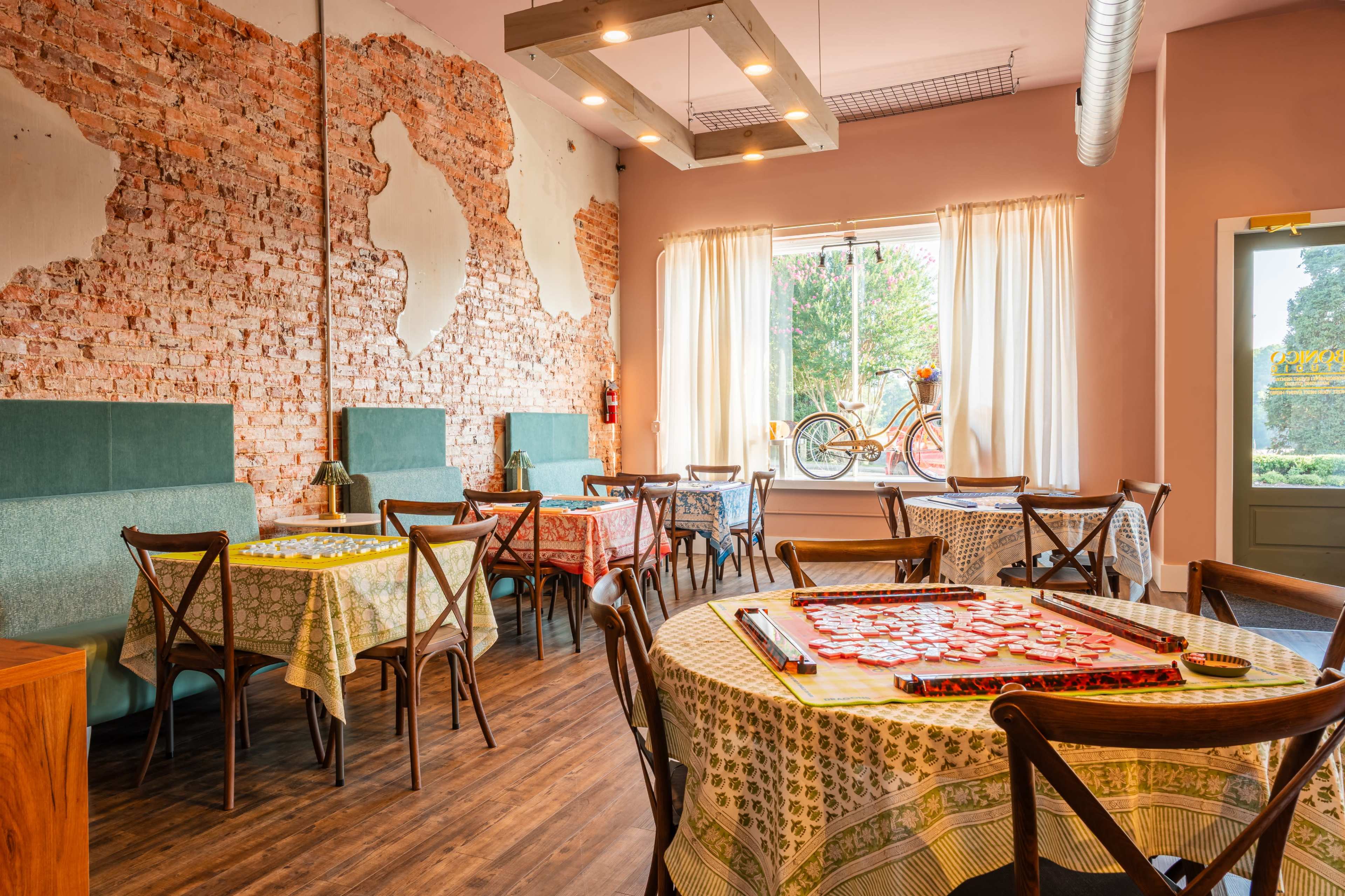The image shows a cozy restaurant interior with rustic brick walls, wooden flooring, and tables covered with patterned tablecloths.