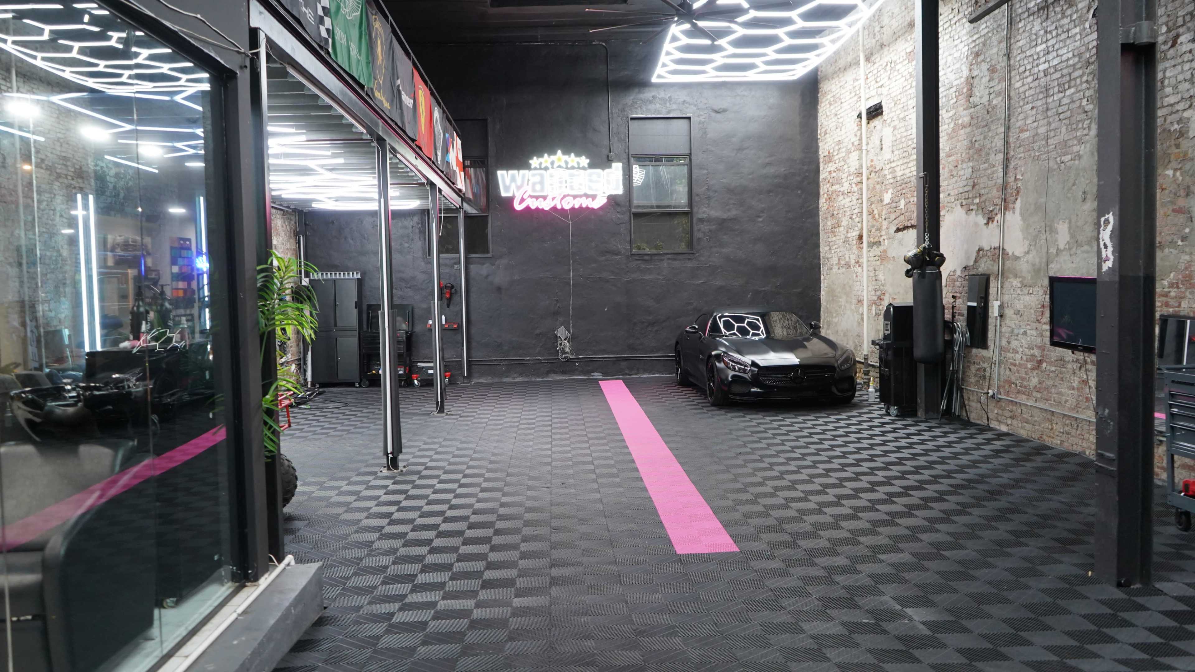 The image shows a modern garage or workshop space with a checkered black and gray floor, featuring a sleek black car parked in the corner and neon lighting above.