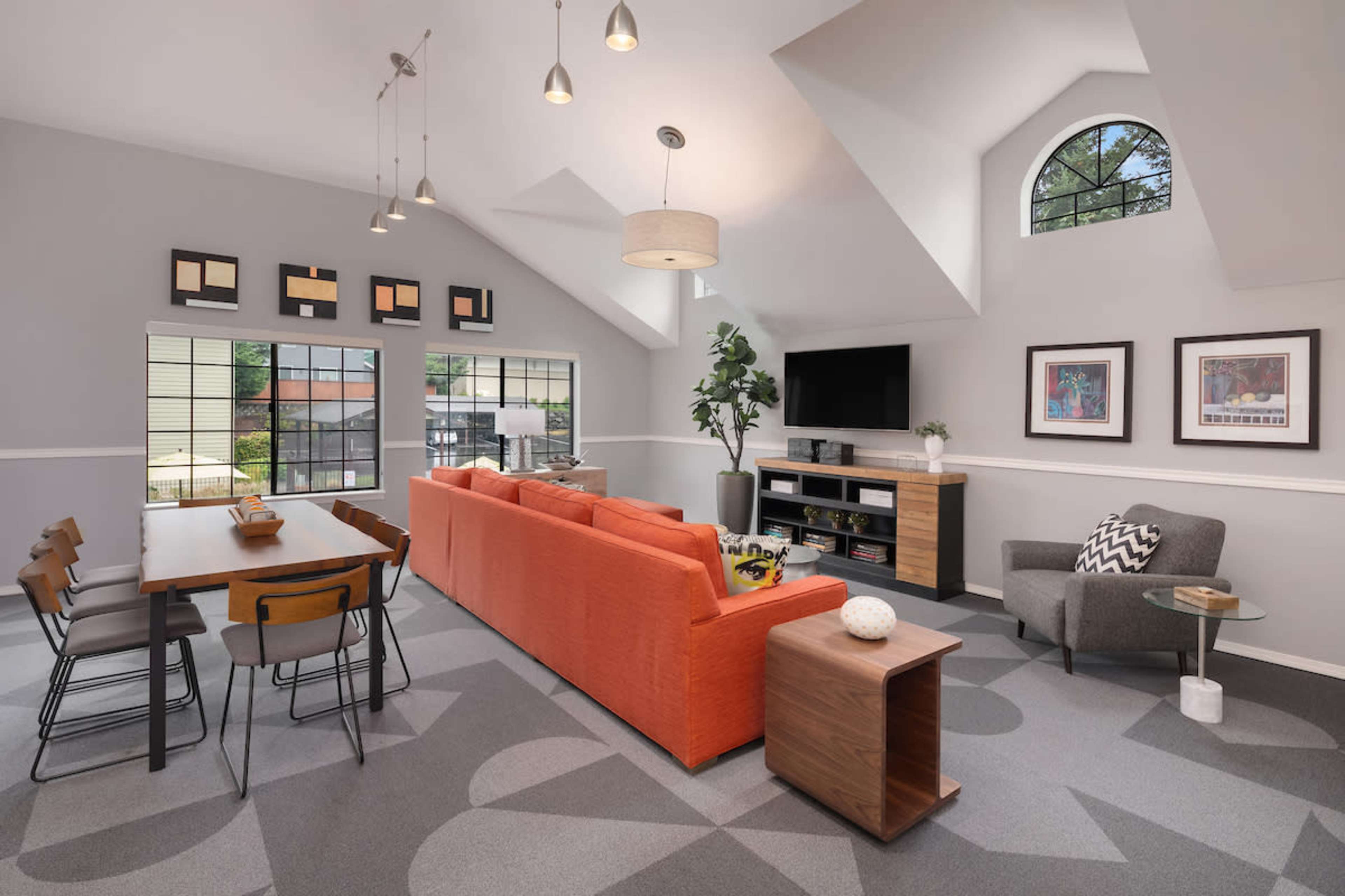 A modern living room and dining area featuring an orange sofa, a dining table with chairs, and a television on a wooden stand under high ceilings with large windows.
