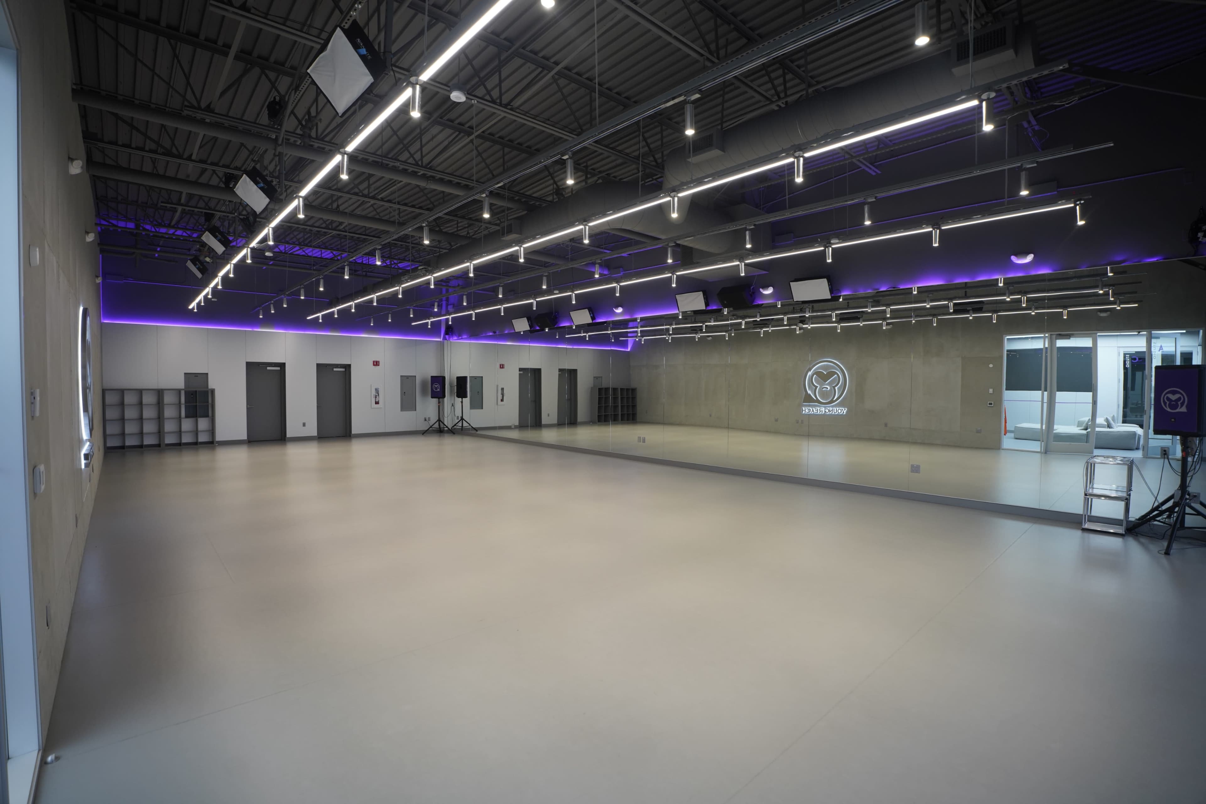 The image shows a spacious and modern dance studio with gray walls, a large mirror, and overhead lighting.