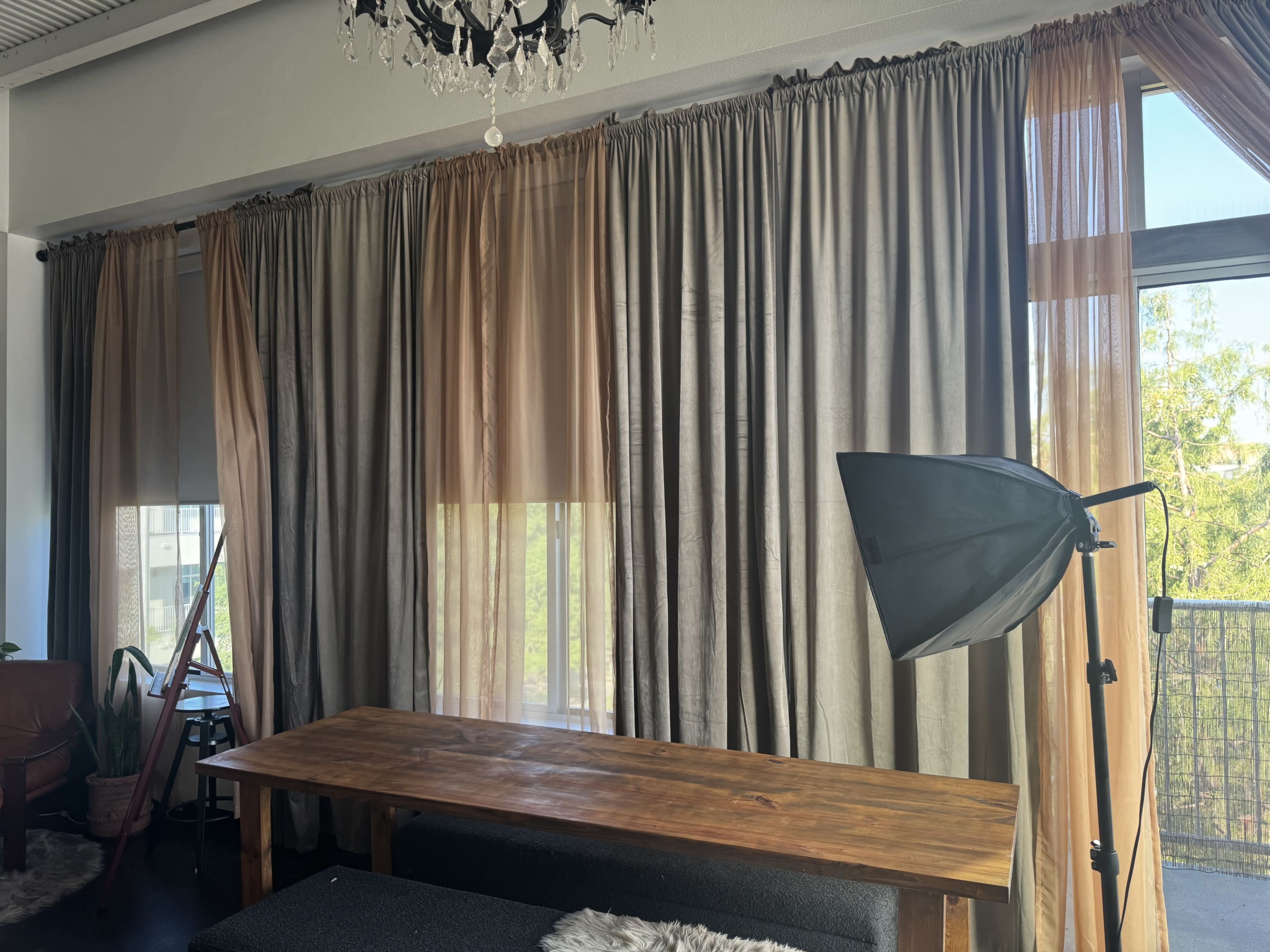 The image shows a modern interior with large curtains, a wooden table, and a softbox light setup near a window.