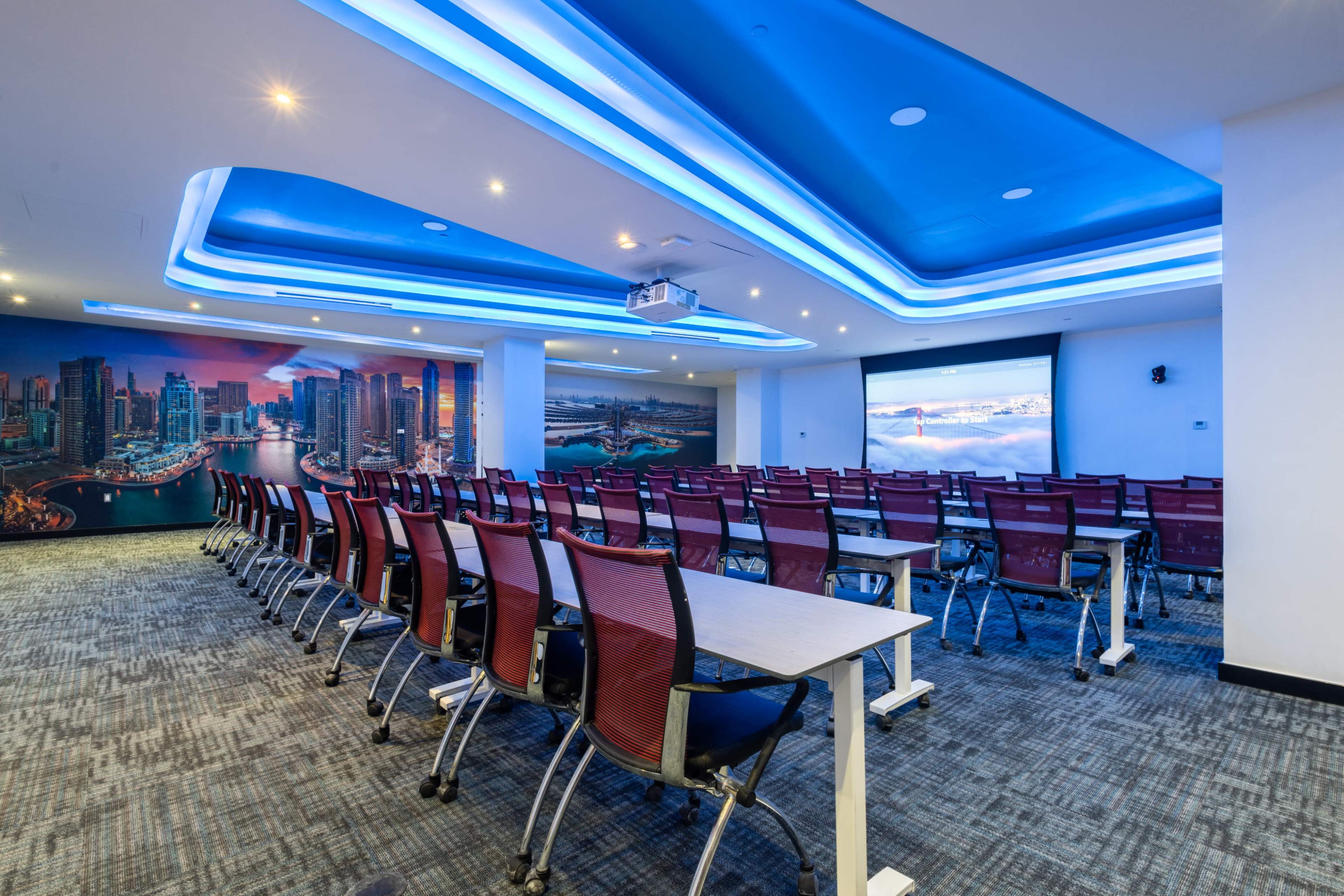 A conference room with rows of chairs facing a projection screen and a decorative wall featuring a city skyline.