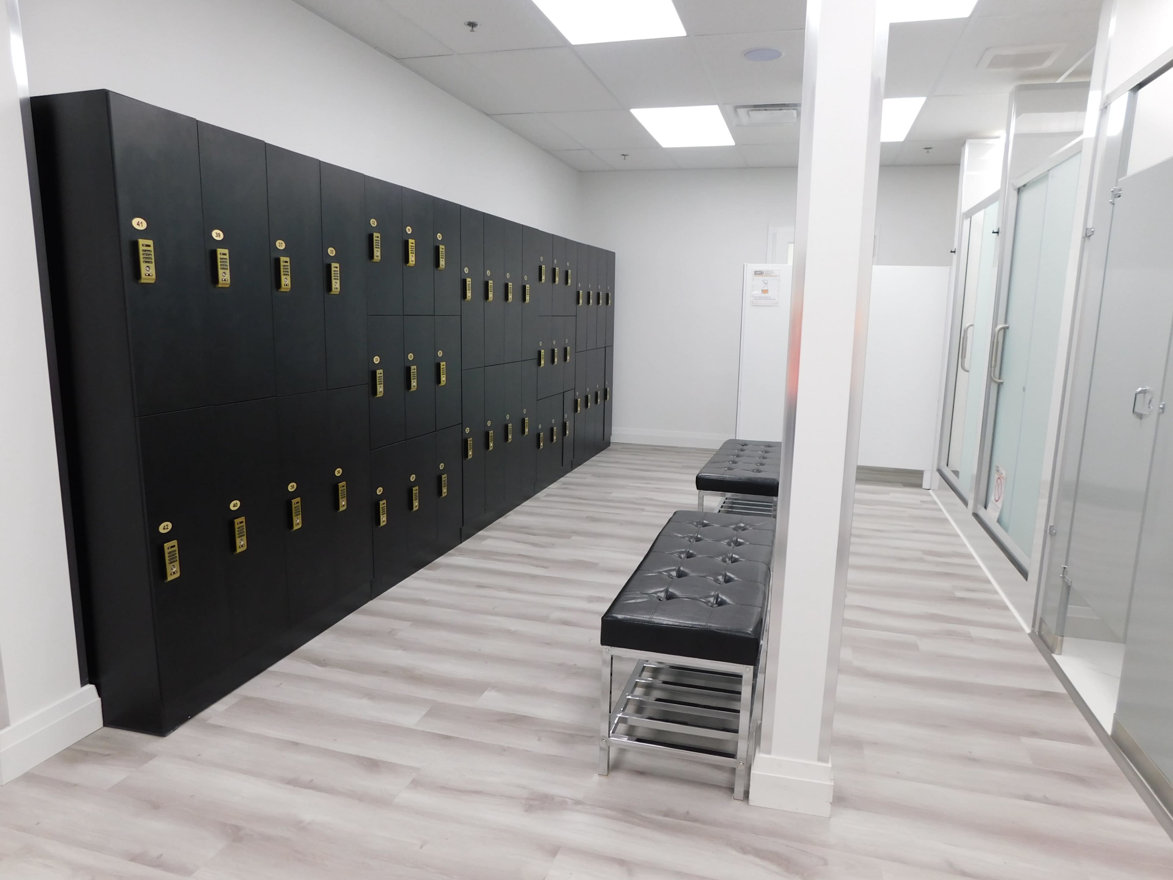 A modern locker room with black lockers along one wall and two cushioned benches facing the lockers.