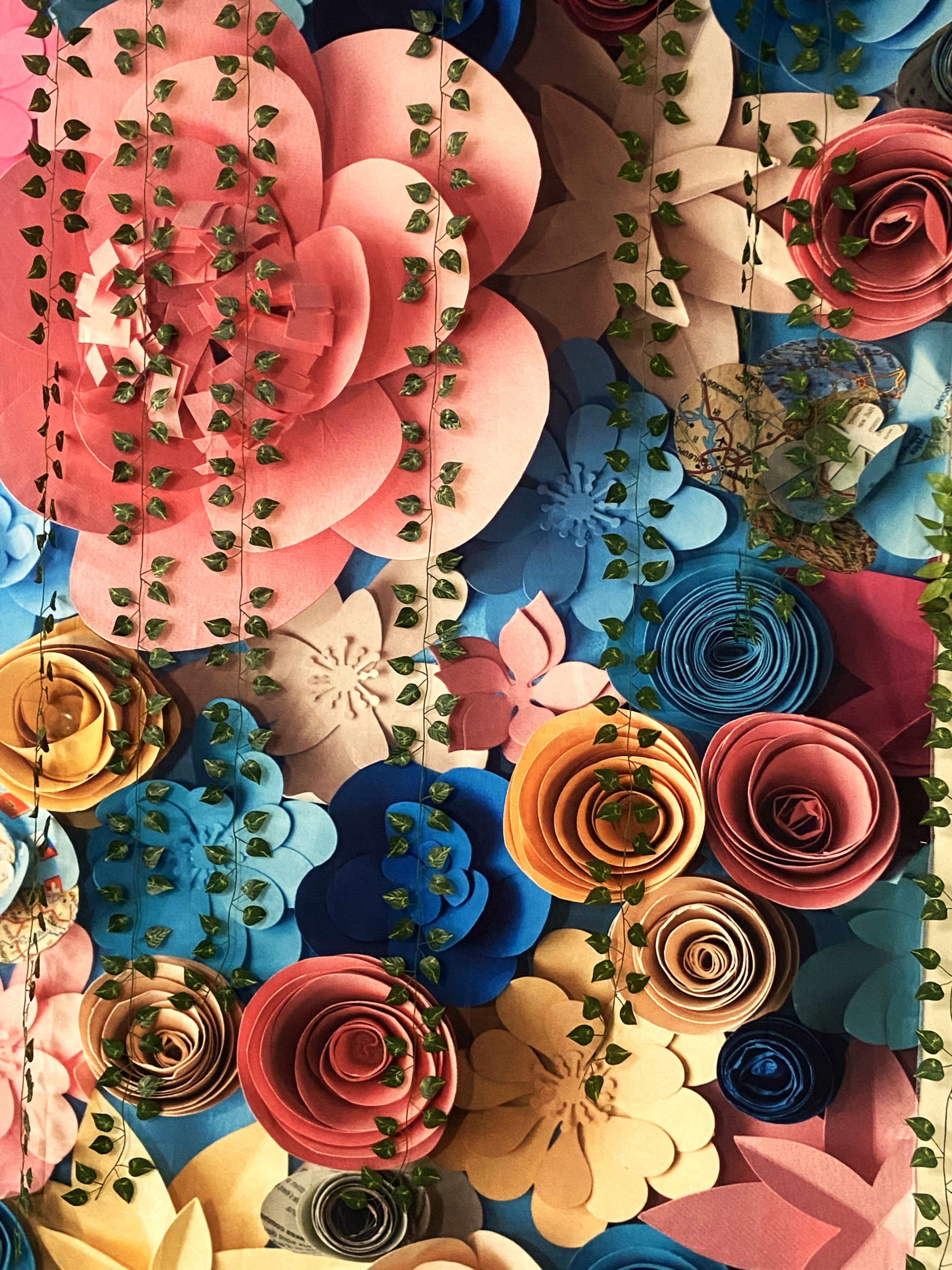 A colorful arrangement of paper flowers and green vines on a textured background.