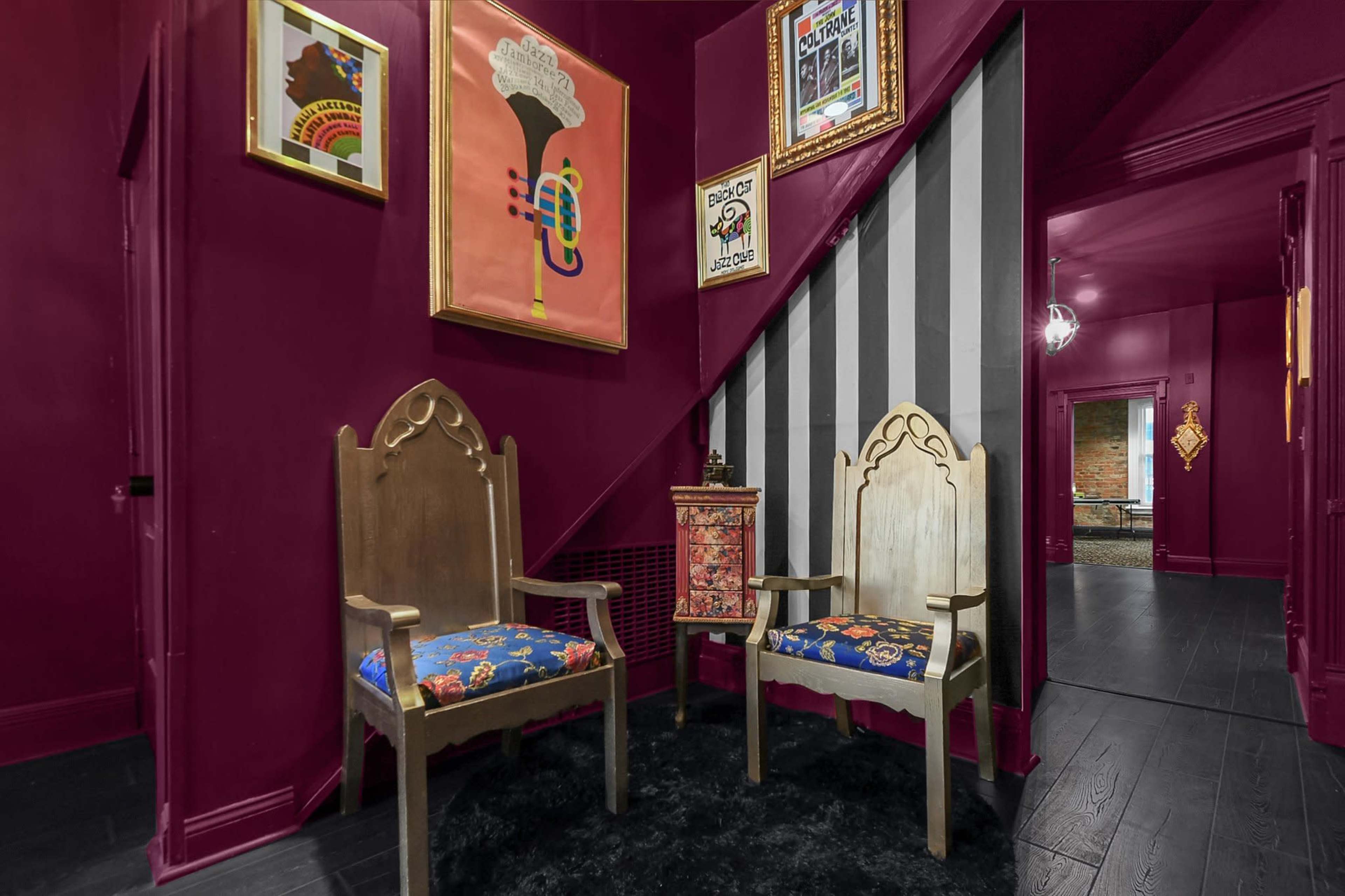 A vibrant purple hallway featuring two wooden chairs with colorful upholstery, a small decorative table, and framed artwork on the walls.