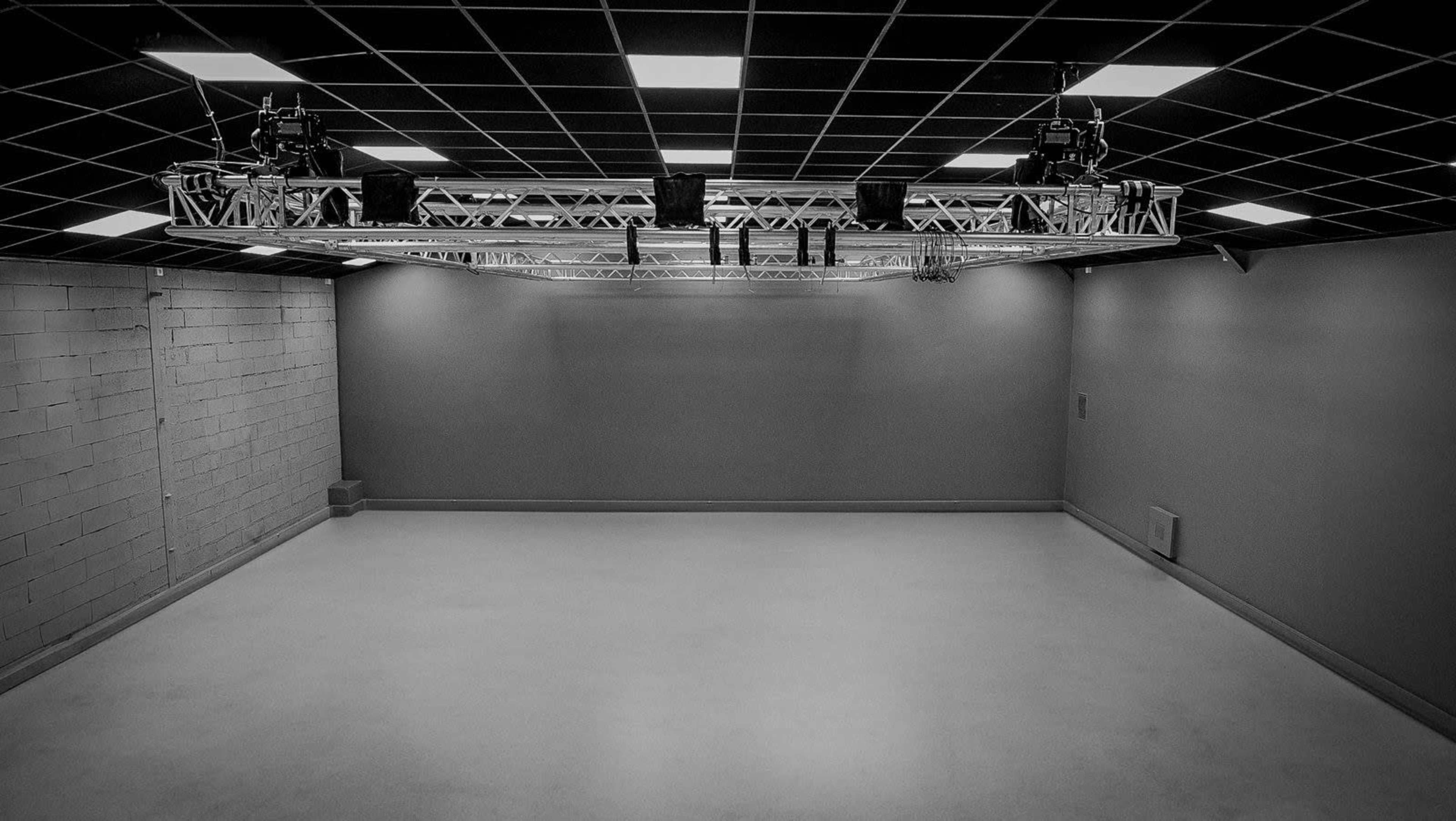 An empty studio space with a grid ceiling and a lighting rig suspended above.