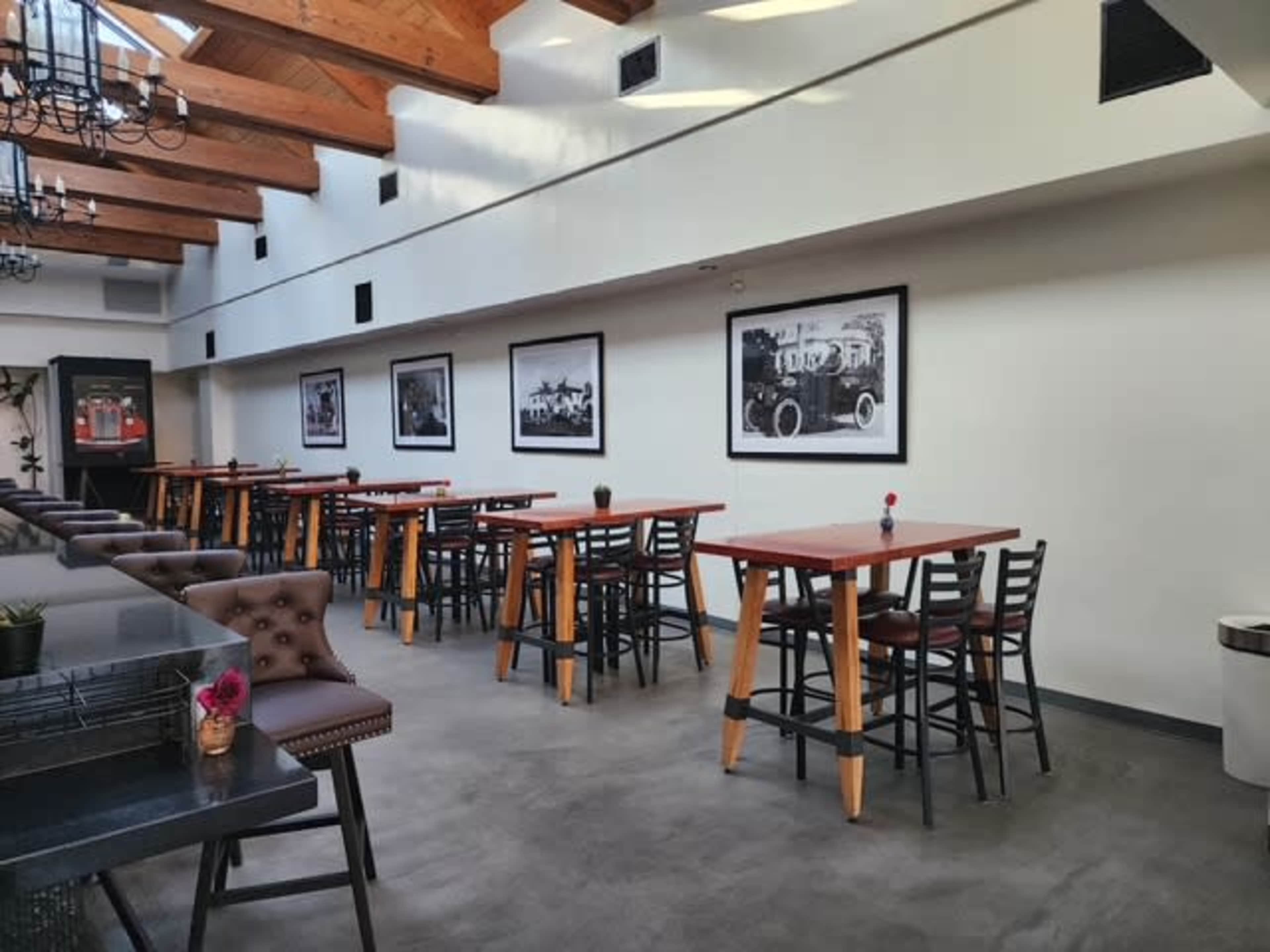 The image shows a bright restaurant interior with wooden beams, empty tables, and framed black-and-white photographs on the walls.