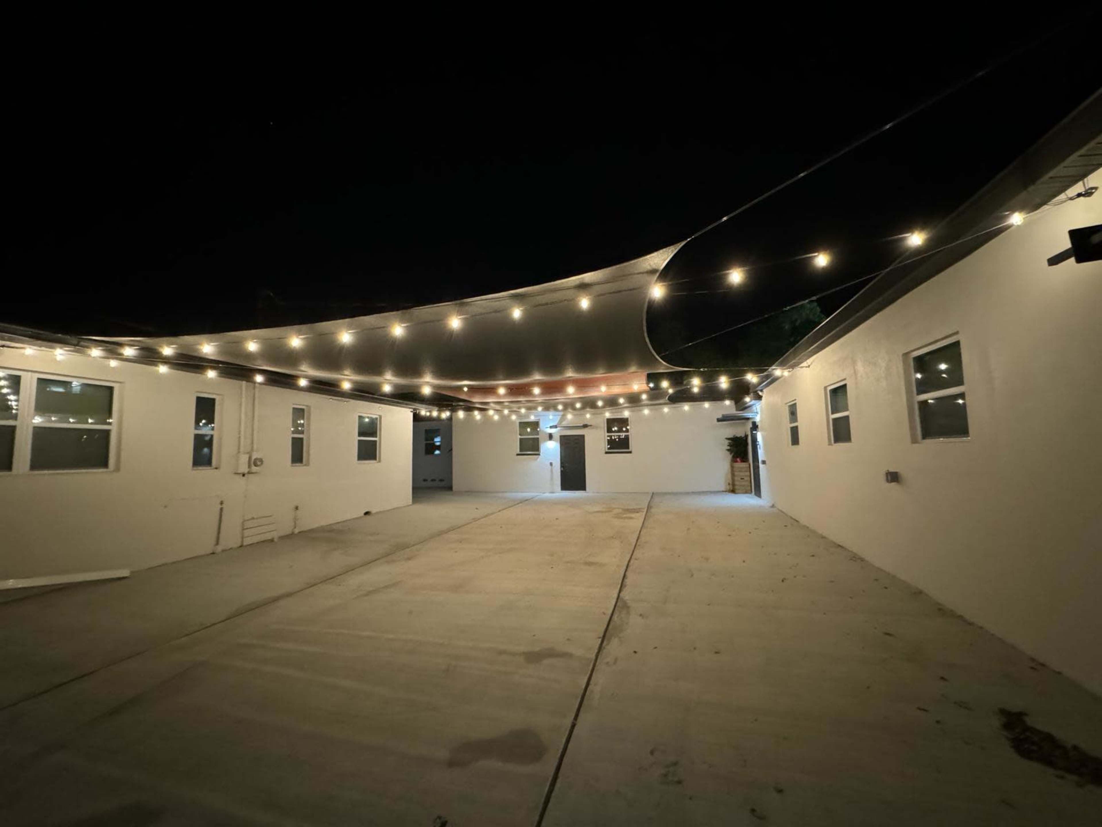 A well-lit courtyard at night features string lights above and white walls surrounding a concrete surface.