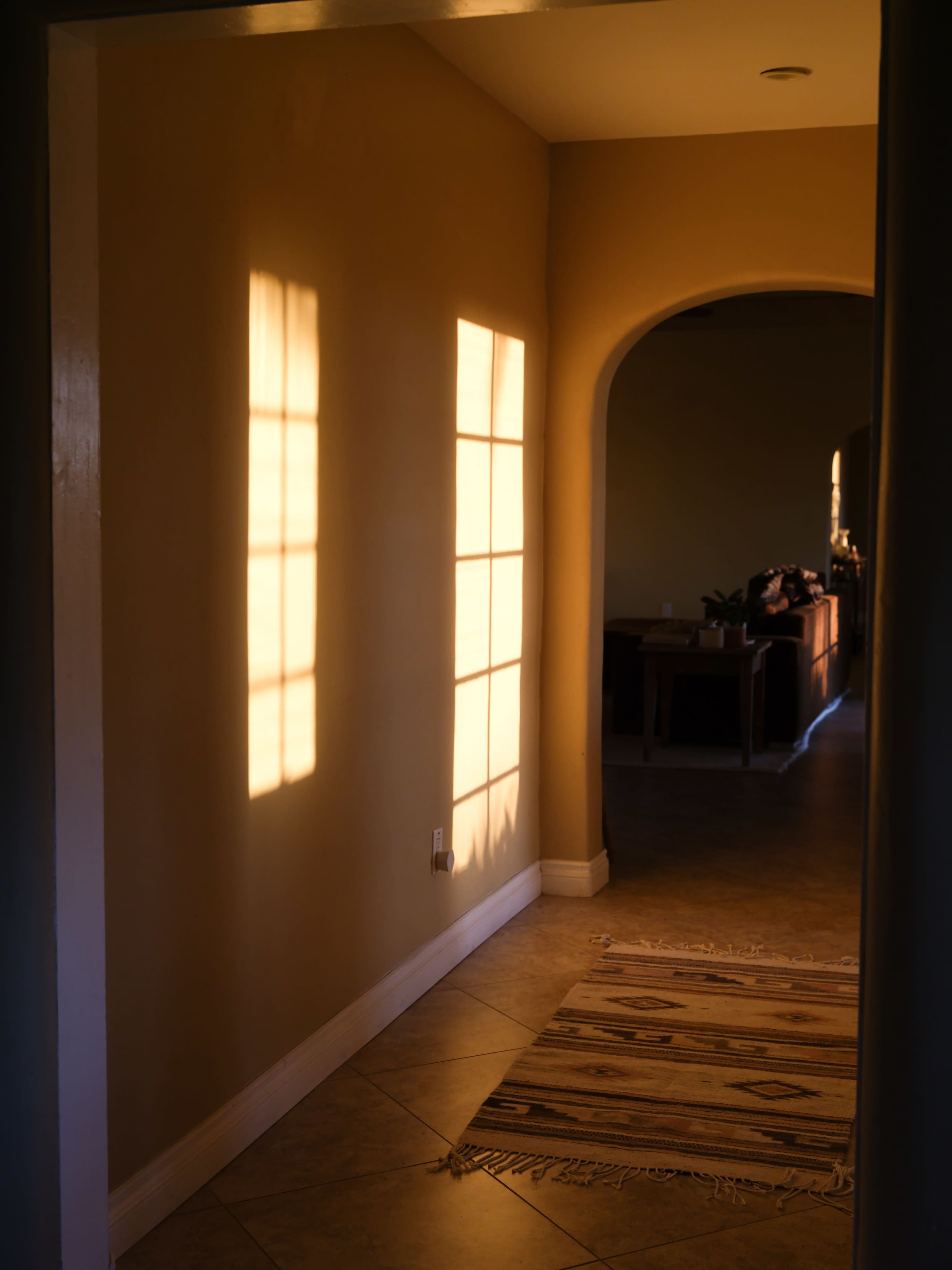 A hallway with a warm-colored wall casts rectangular shadows from a window, illuminated by late afternoon sunlight.