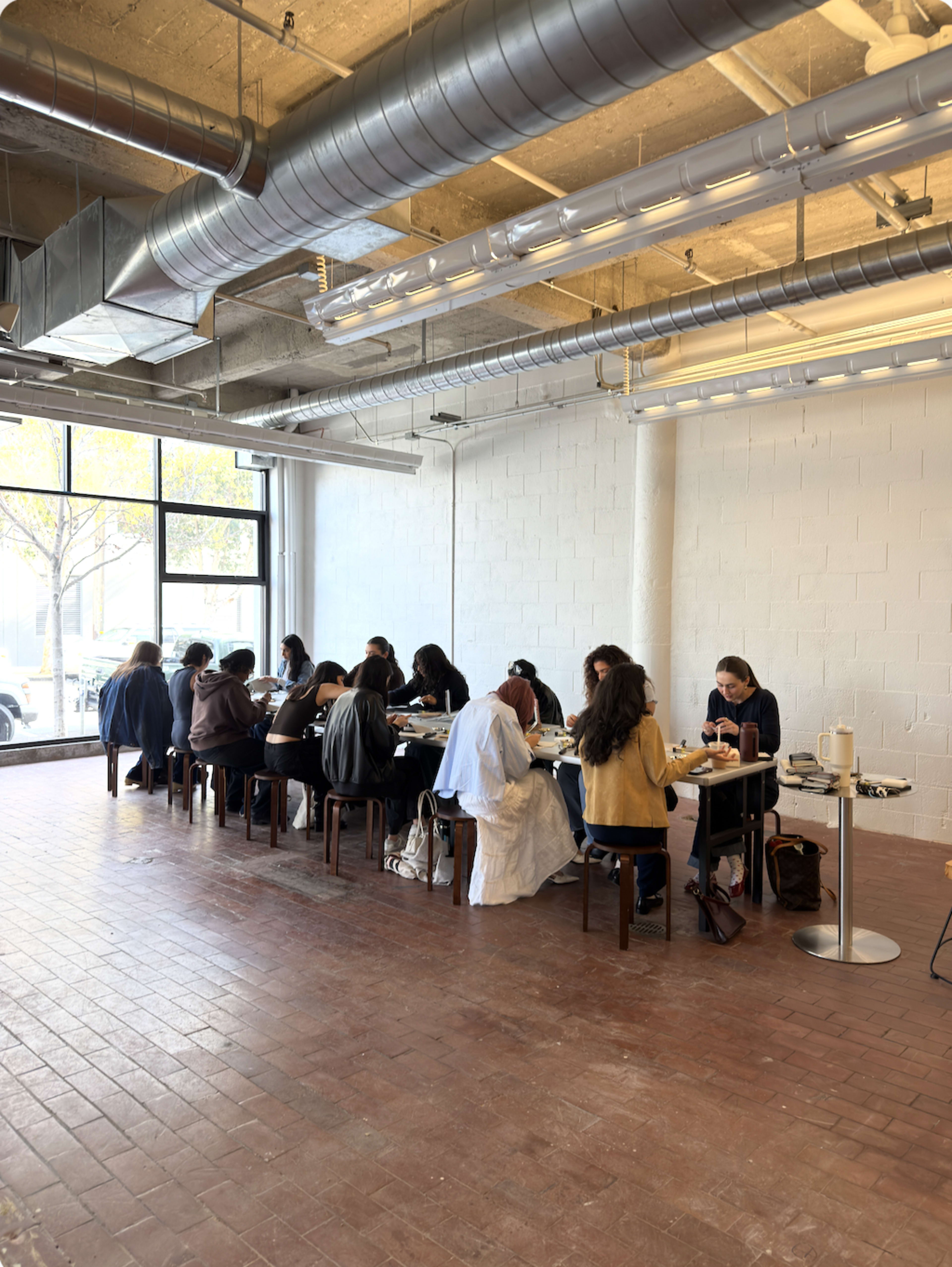 A group of people sits at a long table in a well-lit room with exposed ceilings and large windows.
