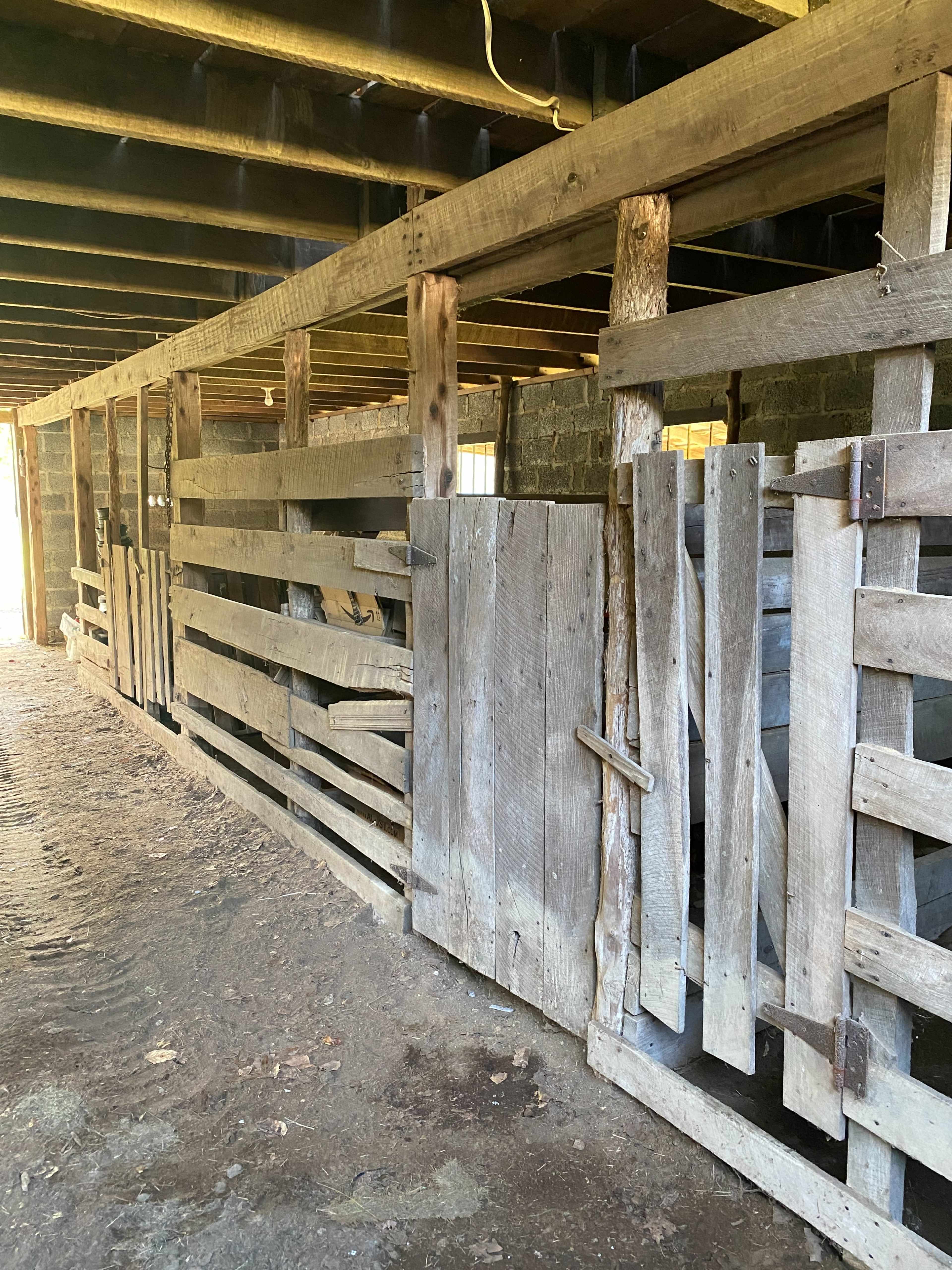 A dimly lit wooden barn interior with several closed stalls made of weathered wooden planks.
