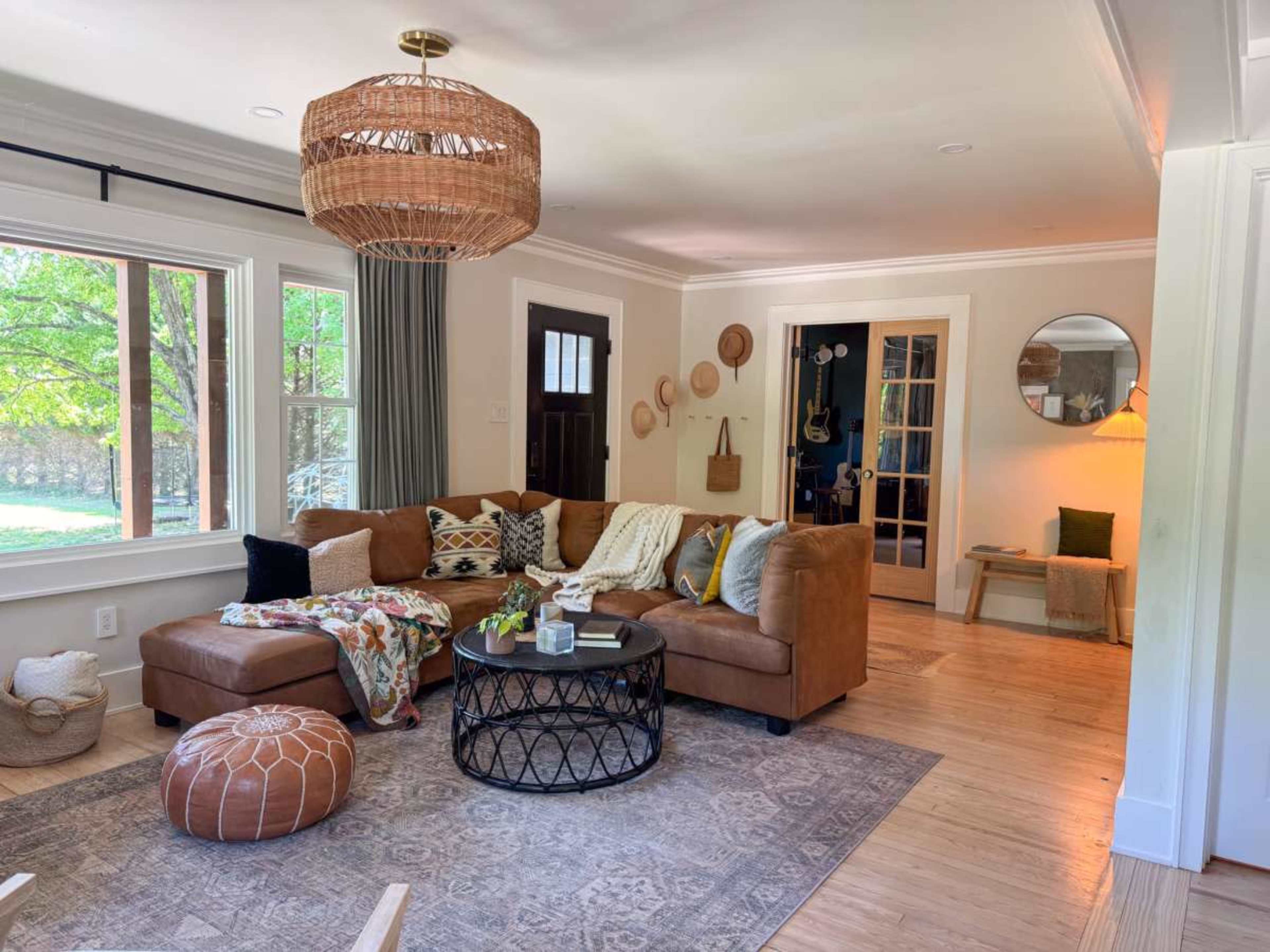 The image shows a cozy living room featuring a large brown sectional sofa, a round coffee table, and decorative items like hats and a circular mirror on the wall.
