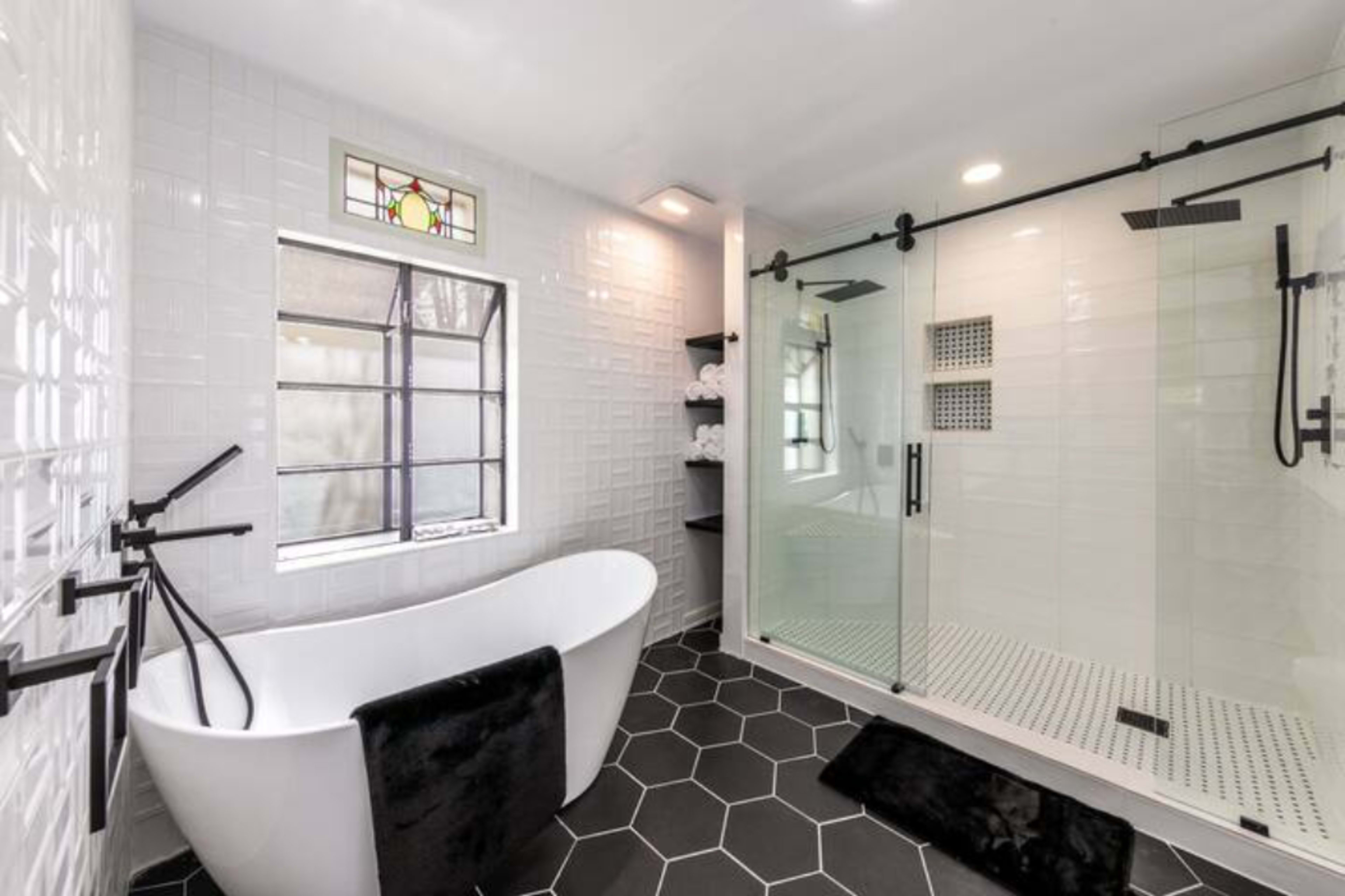 A modern bathroom featuring a freestanding bathtub, a glass shower enclosure, and a large window.