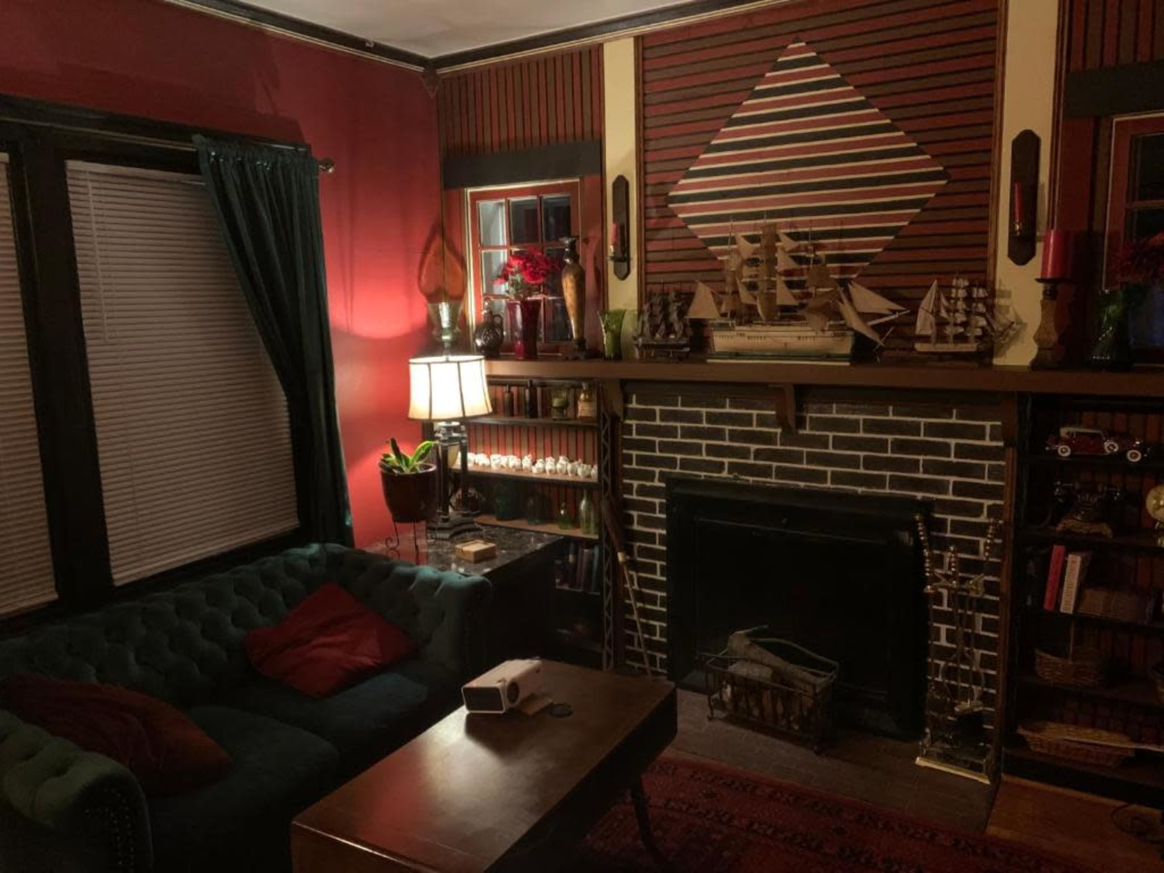The image shows a cozy living room featuring a green tufted sofa, a wooden coffee table, a fireplace with a decorative mantle, and shelves filled with books and decorative items.