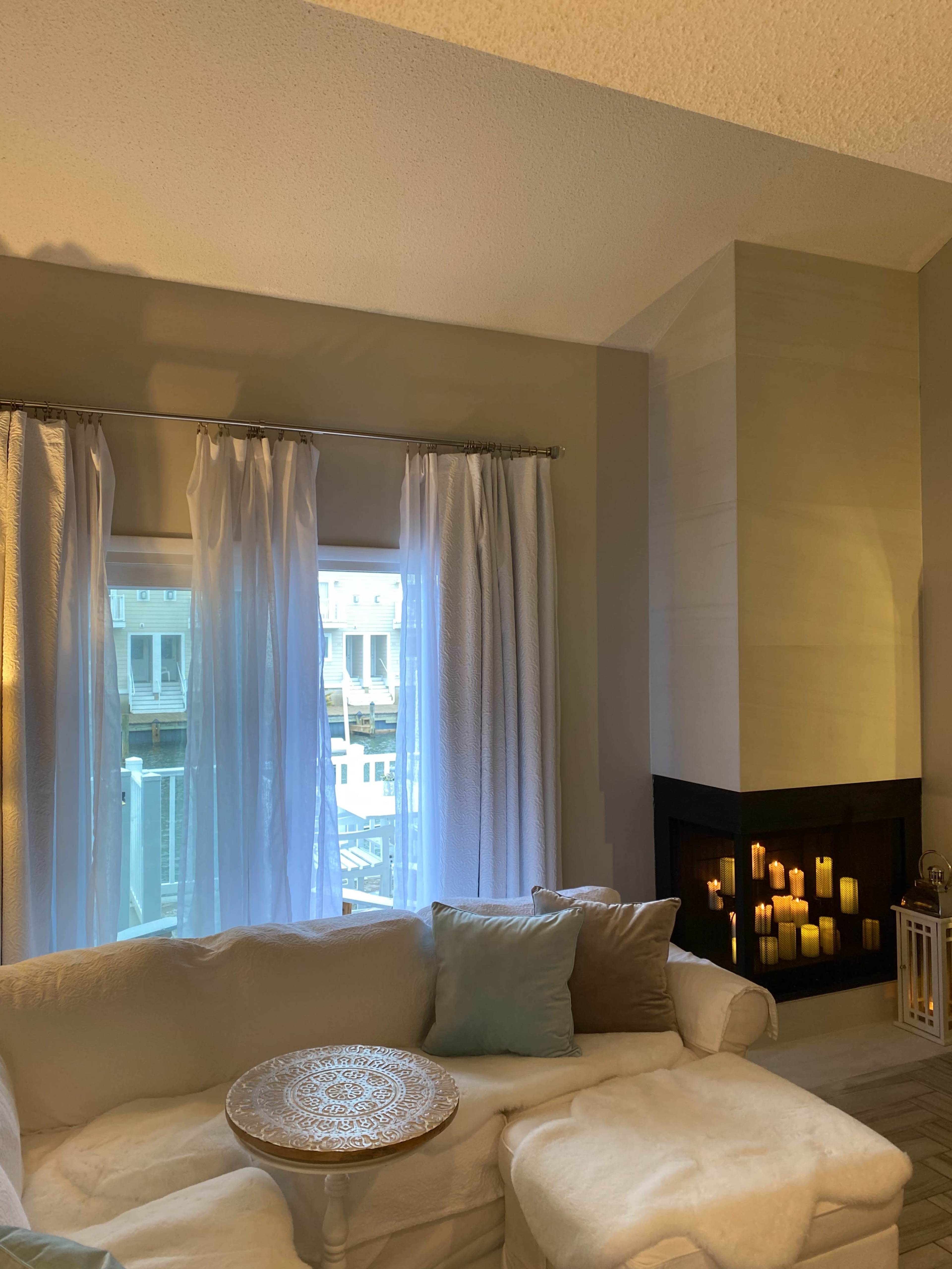 A cozy living room features a white sofa, decorative pillows, and a modern fireplace with candles.