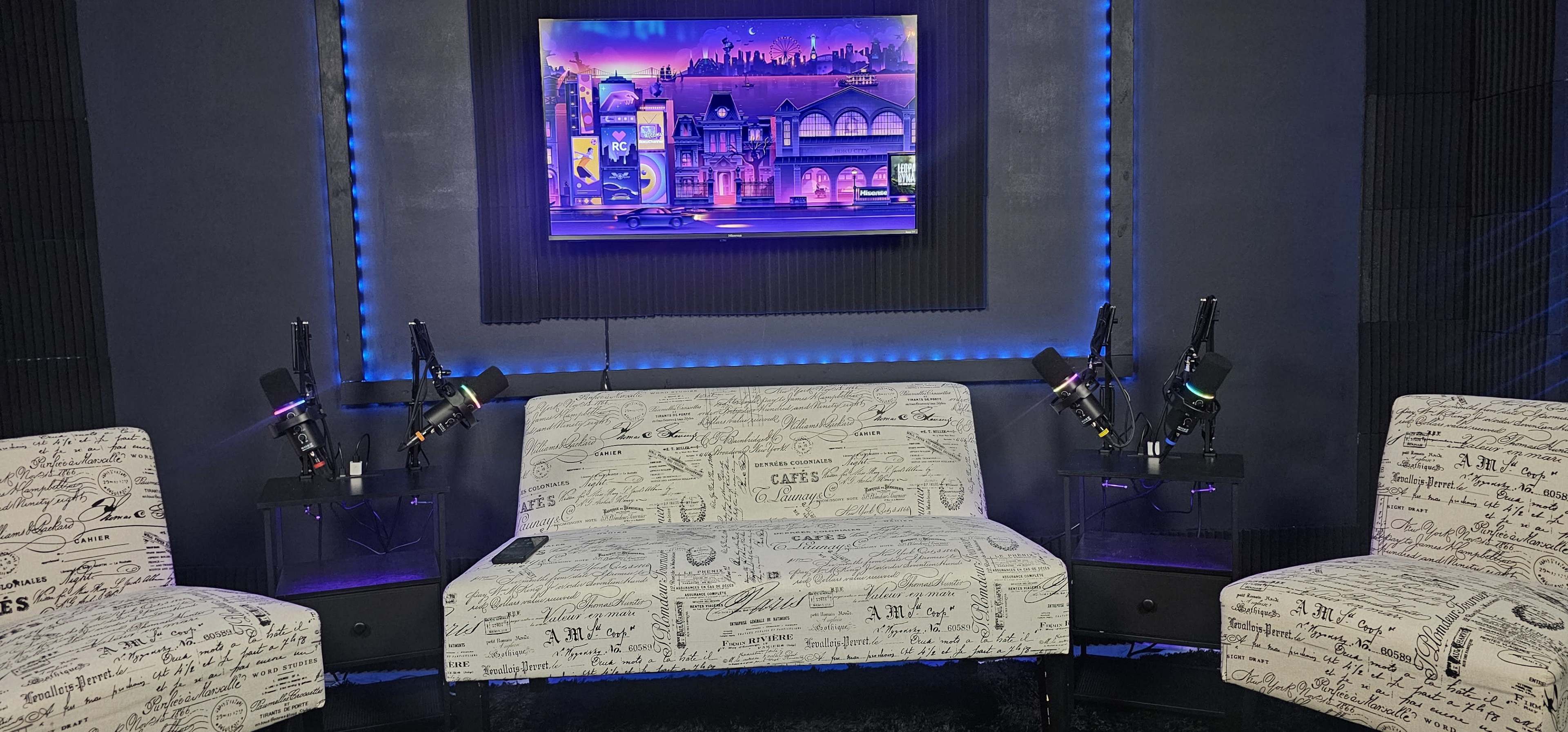 The image shows a modern interview set with a patterned couch, two chairs, and microphones on stands, illuminated by blue LED lights and featuring a colorful wall art piece.