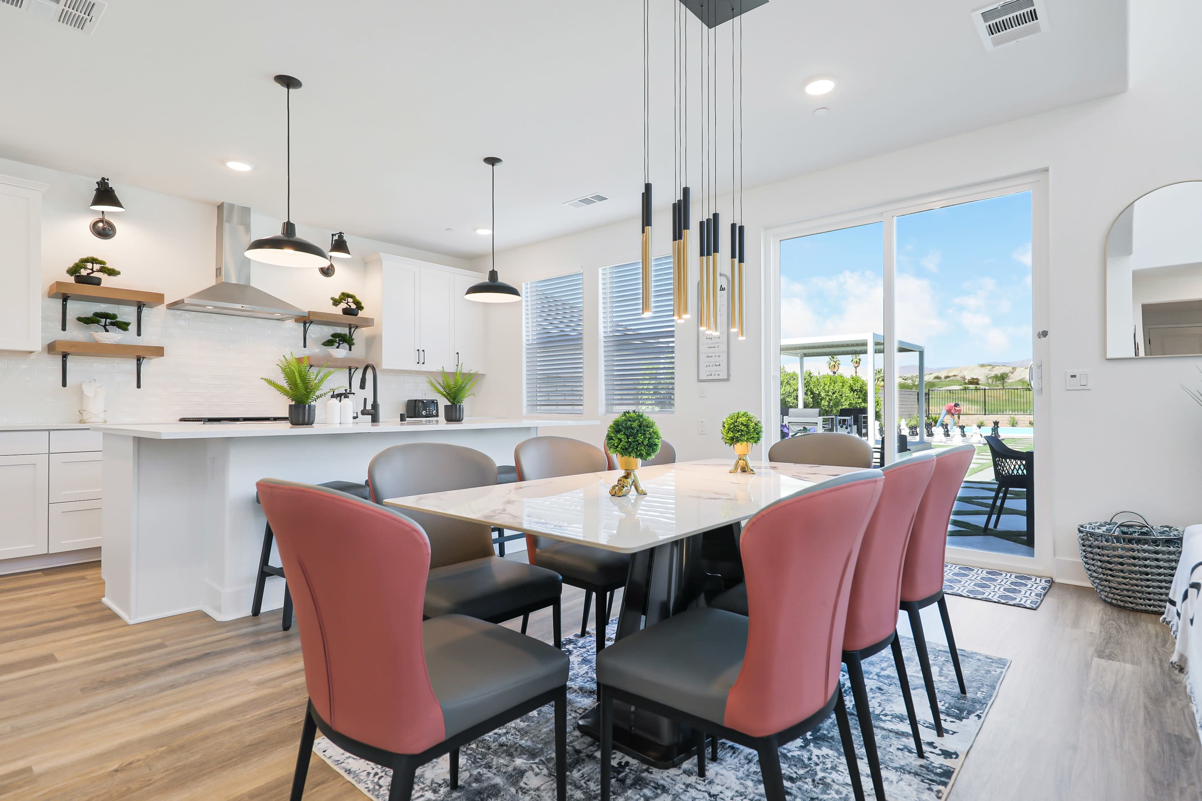 A modern dining area features a white rectangular table surrounded by pink and black chairs, with a large window offering a view of the outdoors.