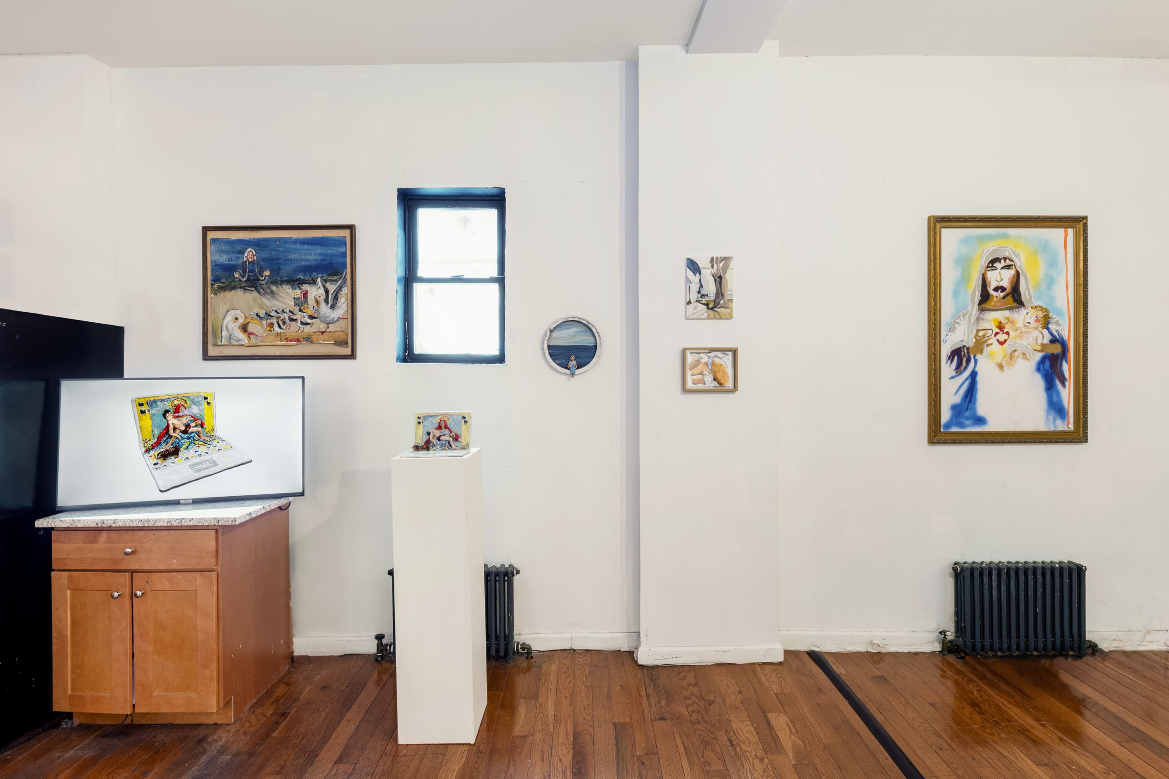 An art gallery room with several paintings displayed on the walls alongside a small pedestal holding a sculpture and a flat-screen monitor on a cabinet.