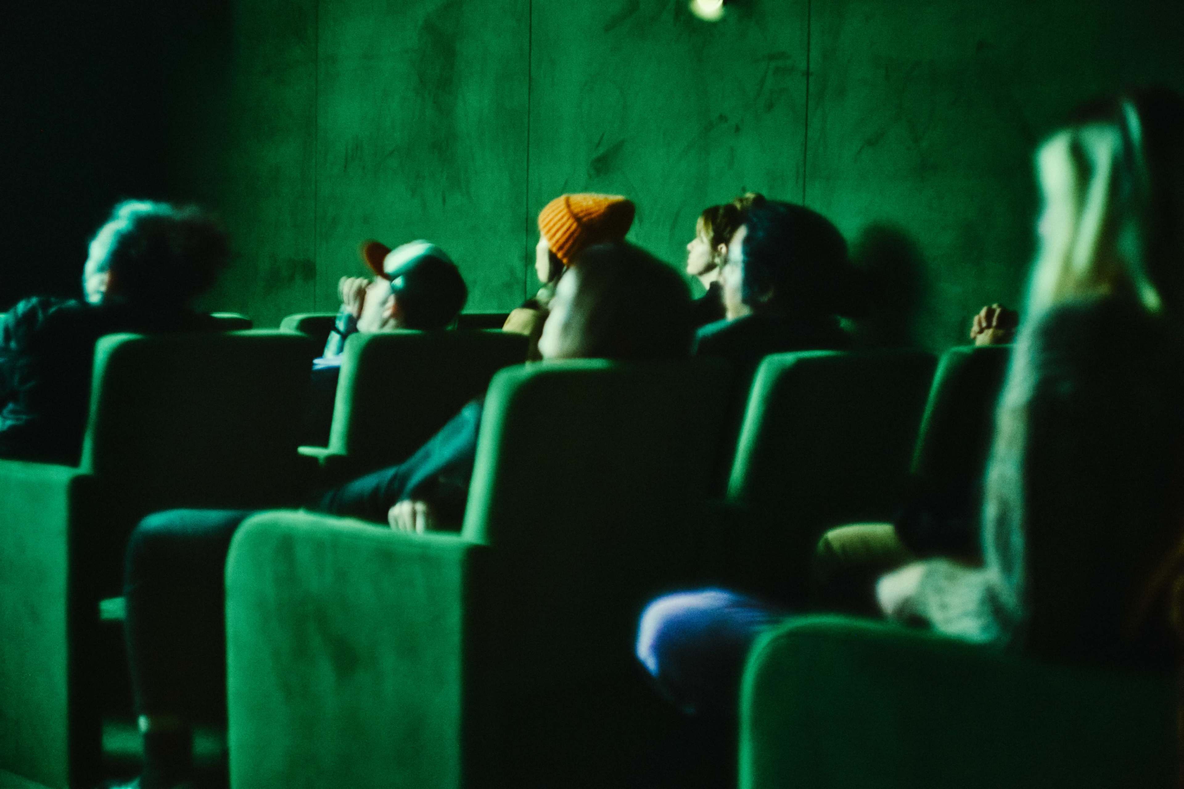 A group of people sits in dimly lit green seats in a theater.