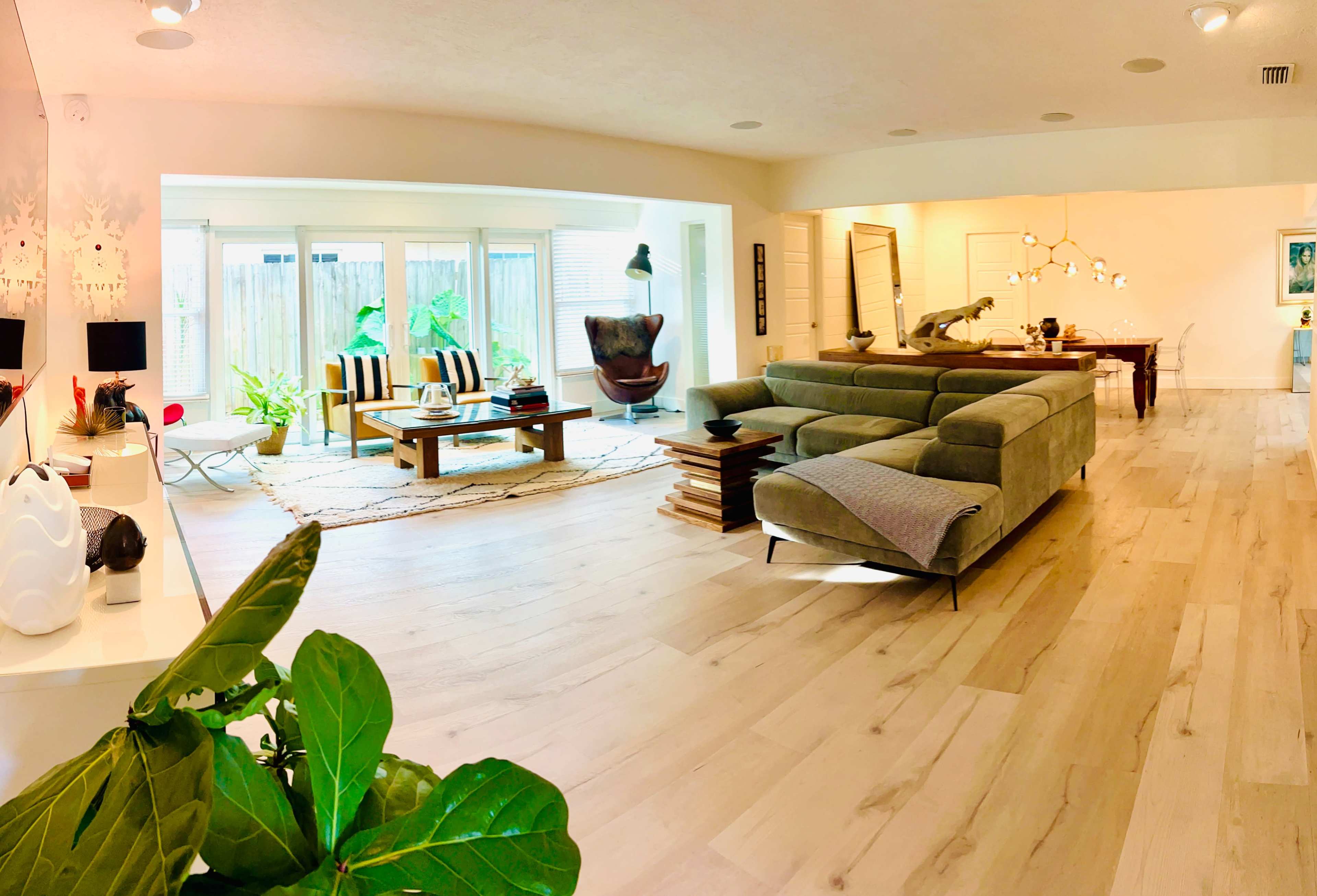 A spacious living area with a seating arrangement of chairs and sofas, a dining table, and large windows allowing natural light.