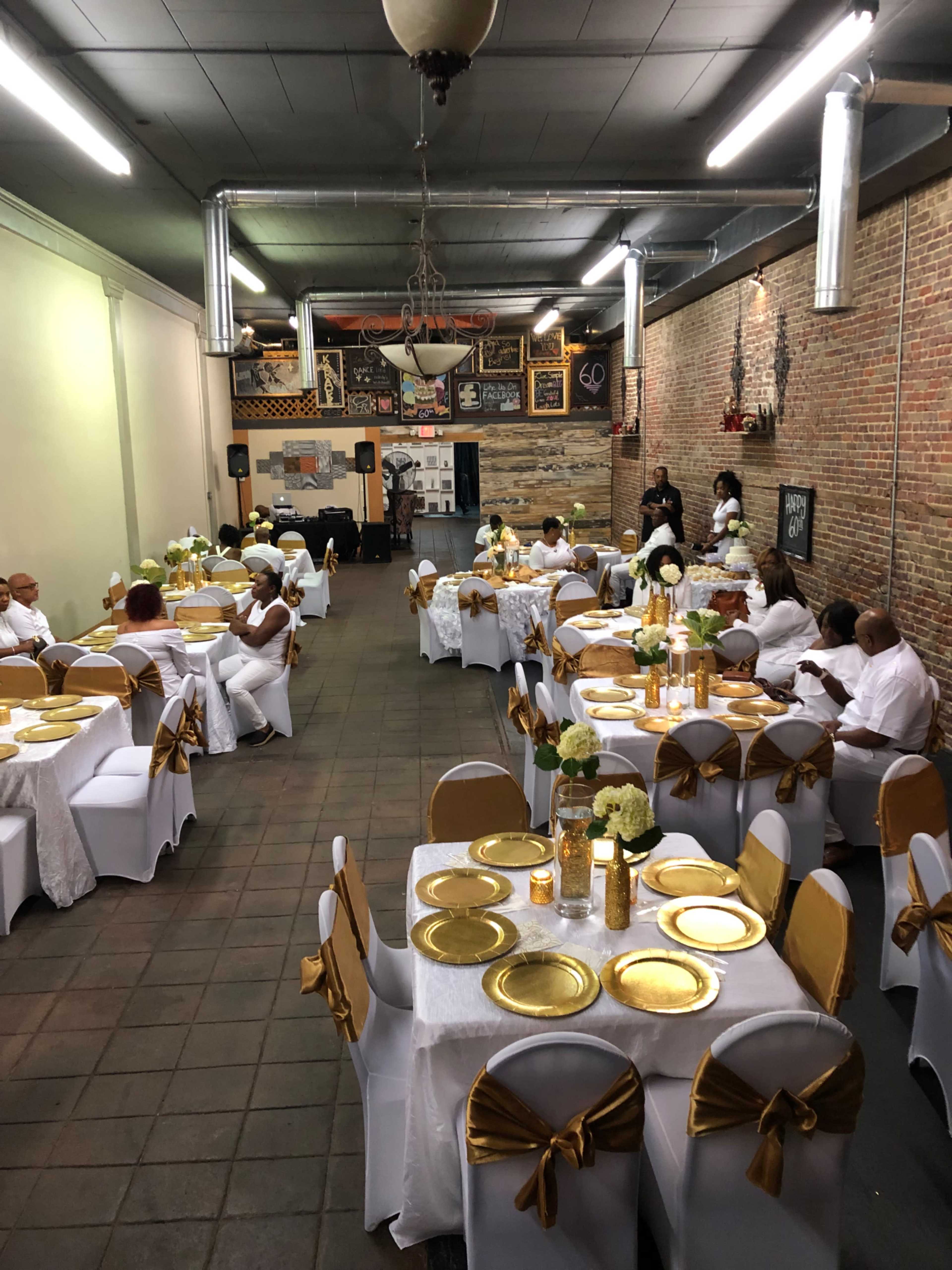 A spacious event hall set for a formal gathering, featuring tables adorned with white and gold decorations.