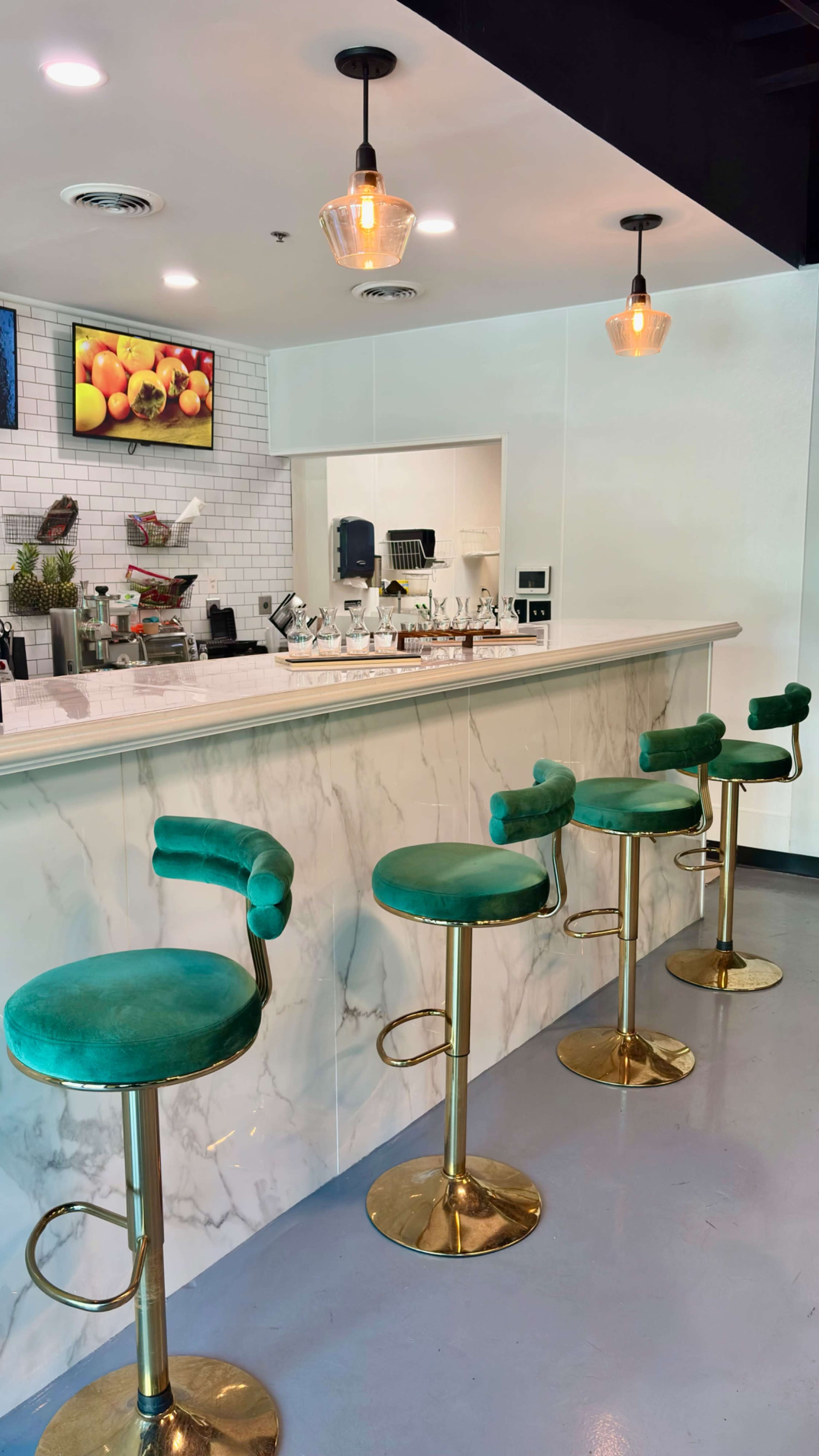 A modern bar featuring a marble counter and four green velvet stools with gold bases.
