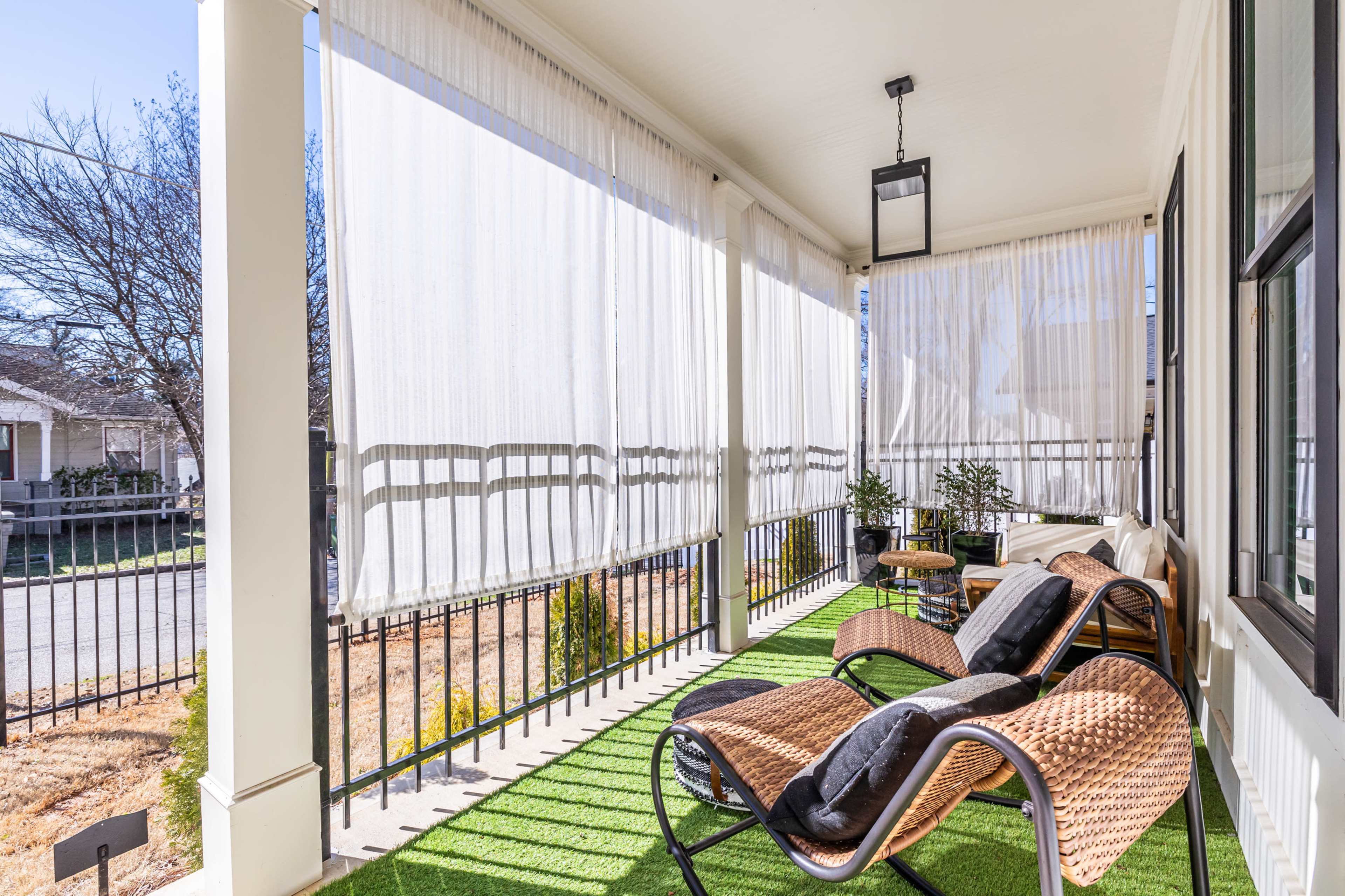 The image shows a porch with two lounge chairs, green grass carpet, sheer white curtains, and a small coffee table.