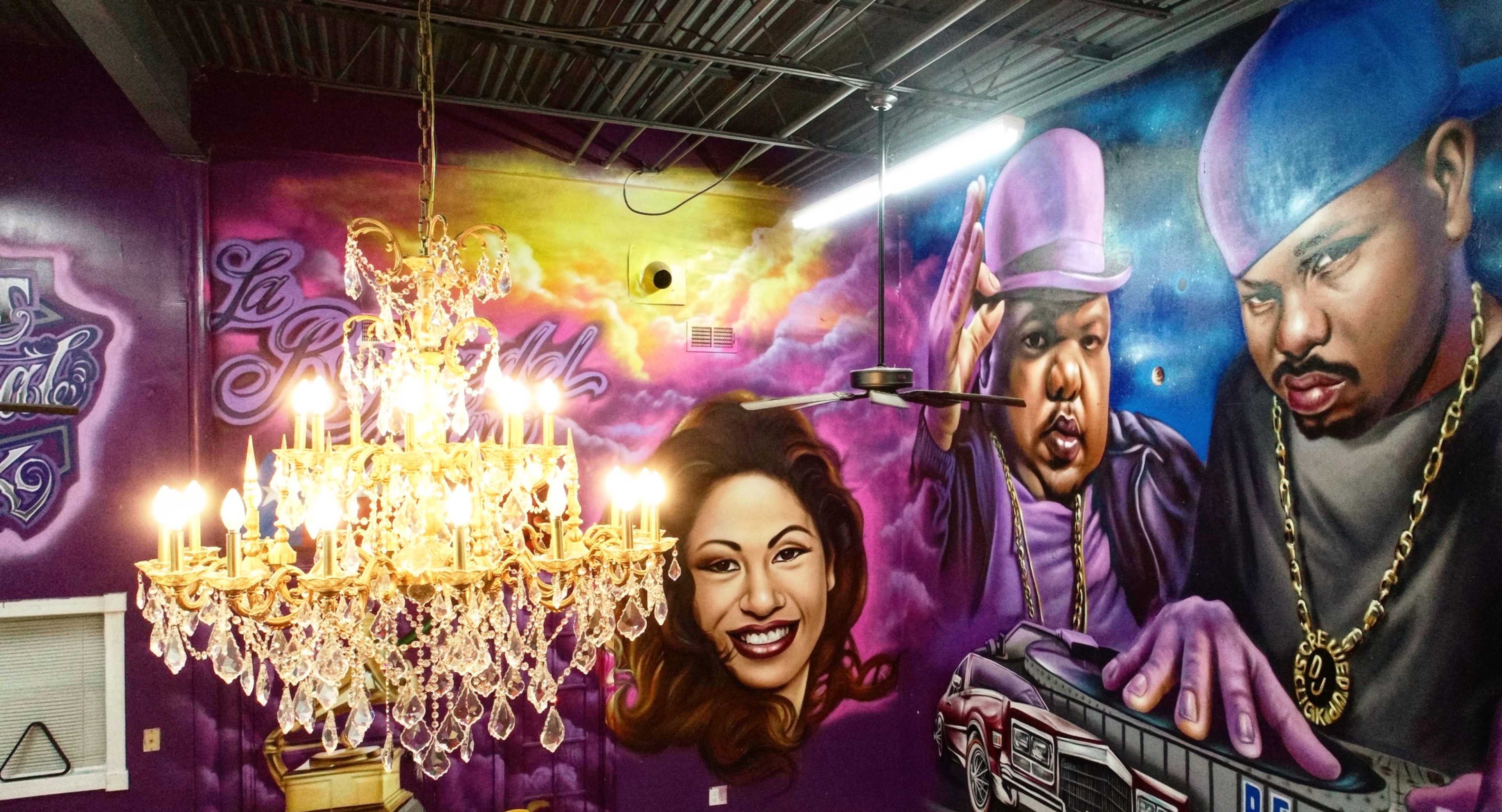 A vibrant mural on a purple wall featuring portraits of individuals alongside a chandelier, set in an indoor space.