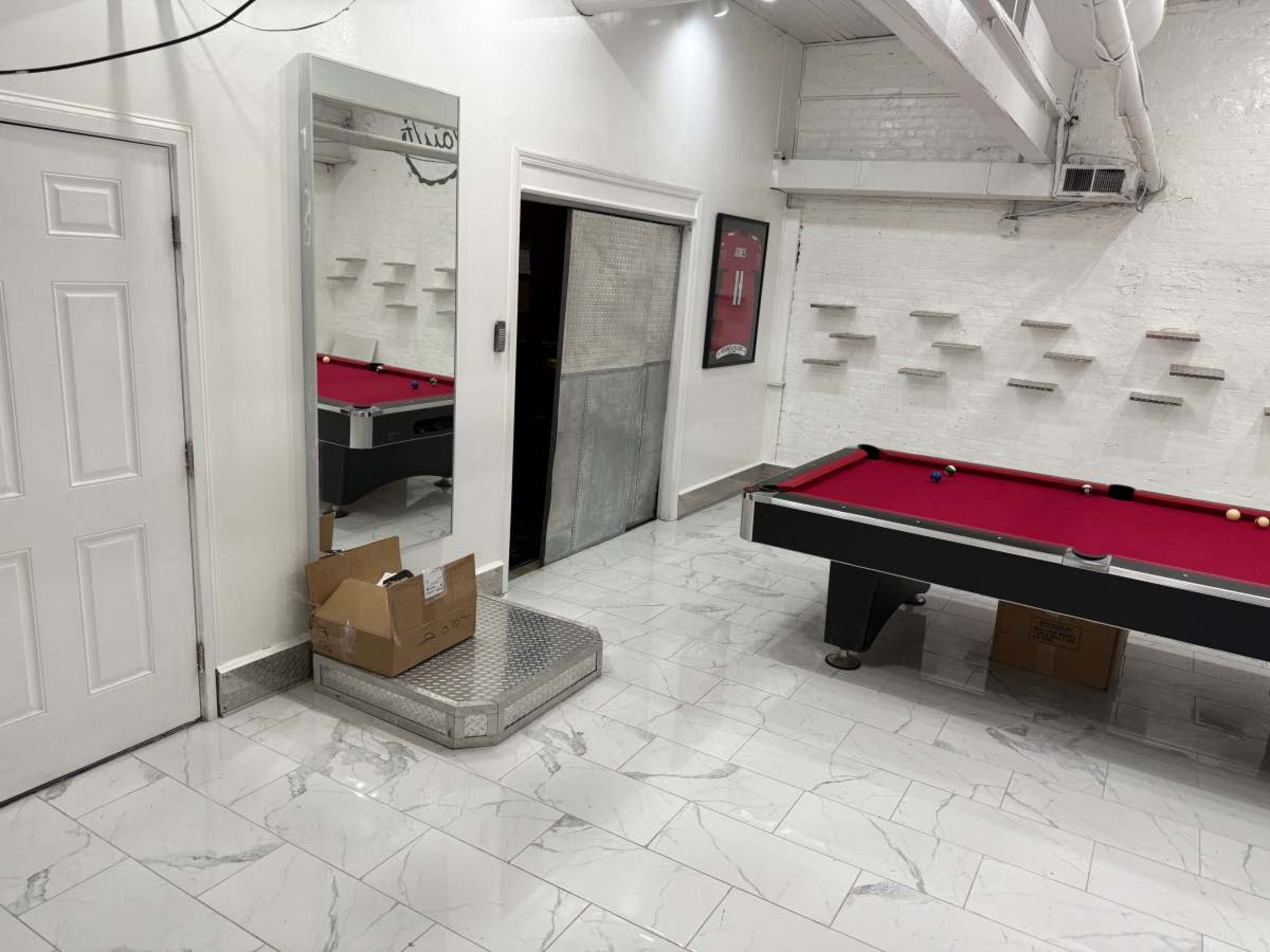 The image shows a room with a red pool table, a large mirror, and a doorway leading to another space, featuring white walls and marble flooring.