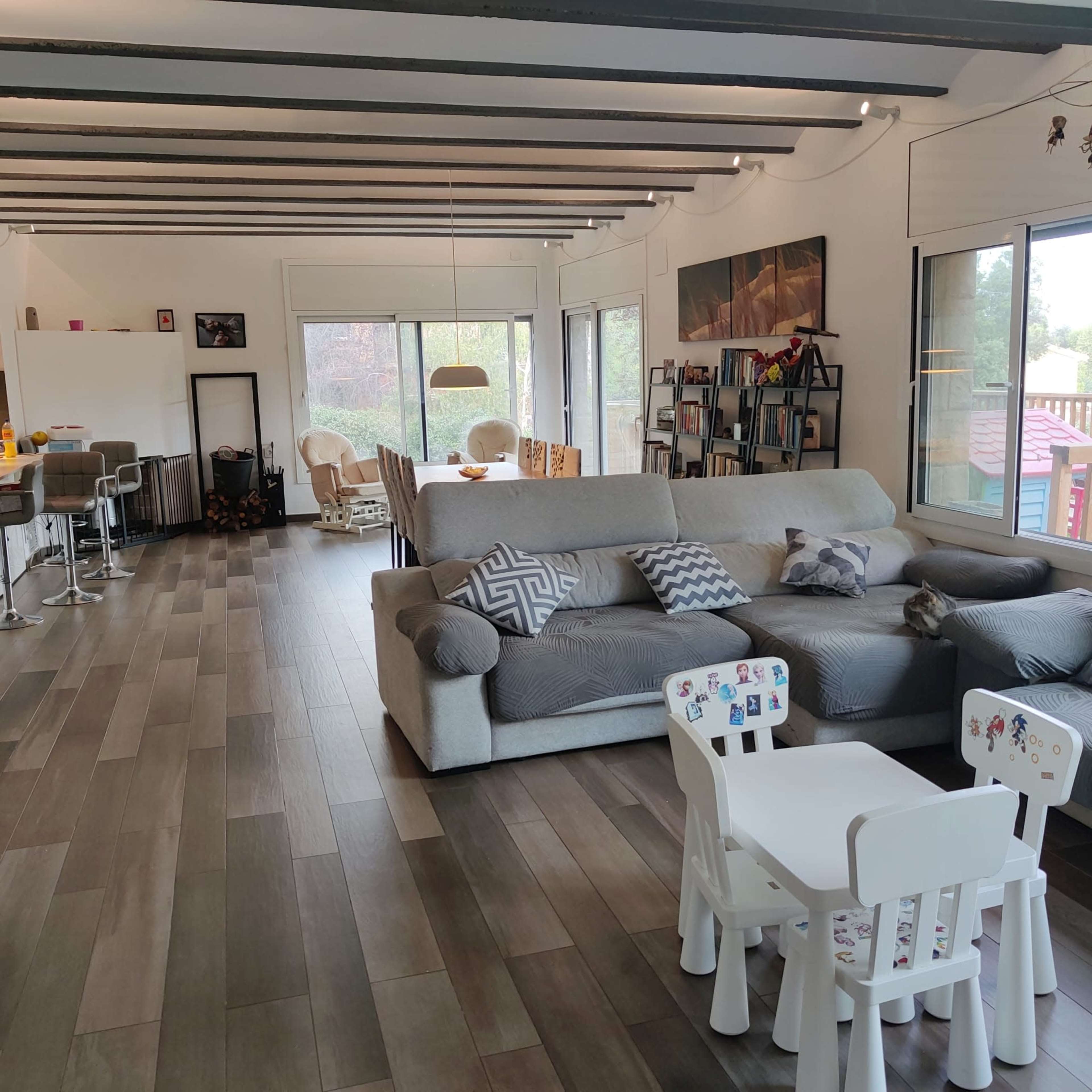 A spacious living area with a large sofa, a dining area with chairs, and a children's table set on tiled flooring.