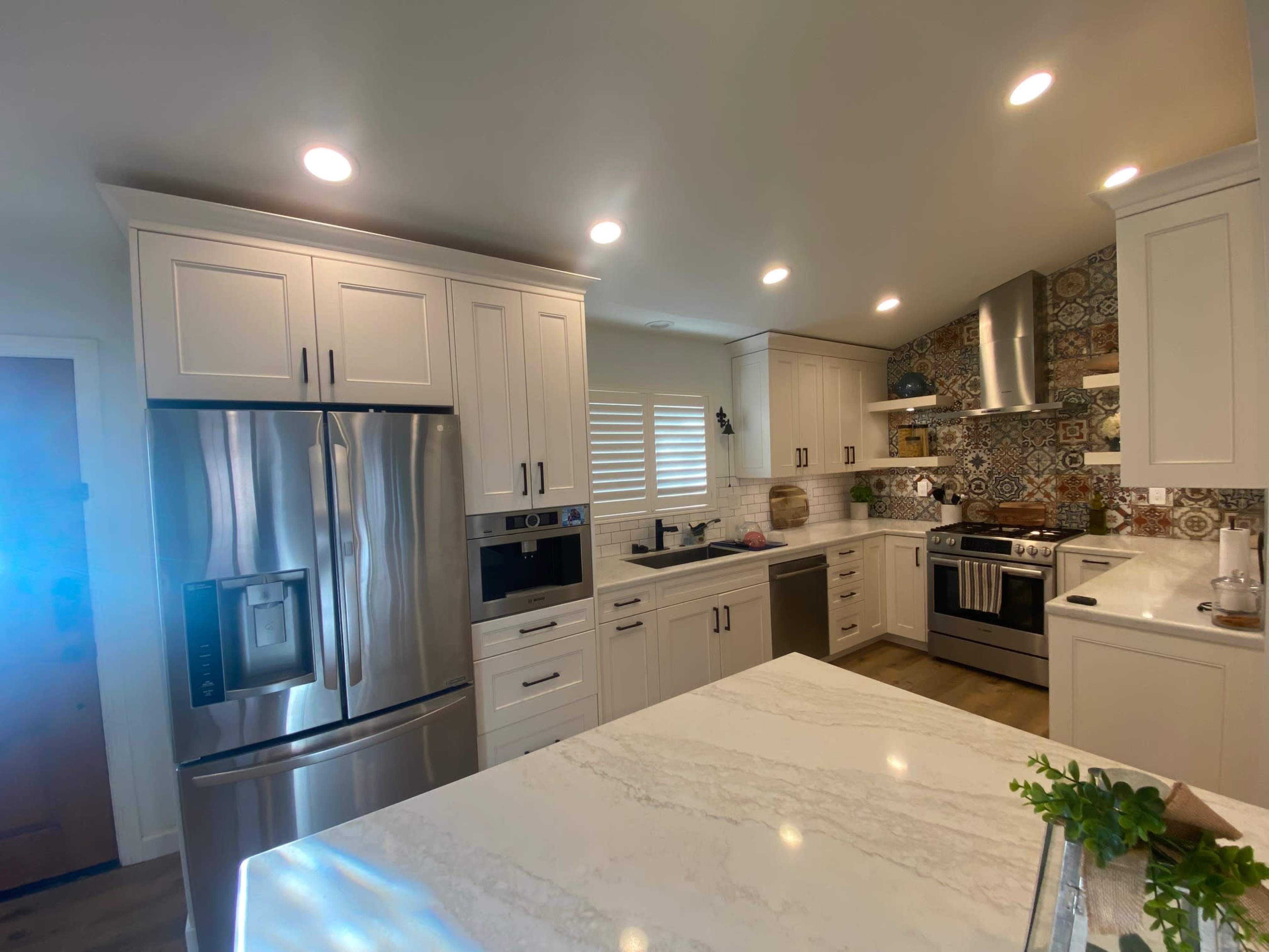 The image shows a modern kitchen featuring white cabinetry, stainless steel appliances, a marble countertop, and a patterned tile backsplash.