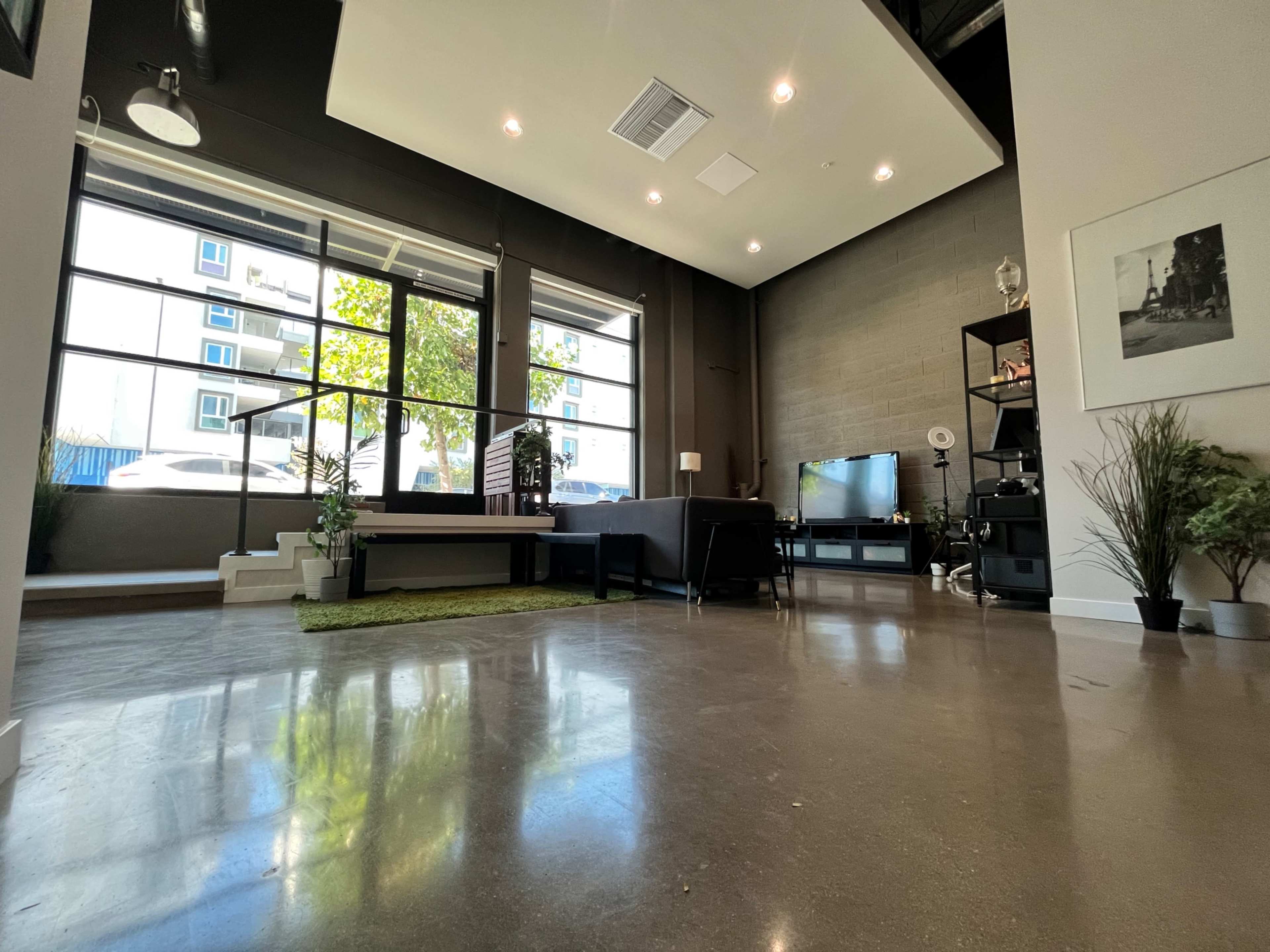 A modern, spacious interior with large windows, a polished concrete floor, and various furnishings, including a desk and a television.
