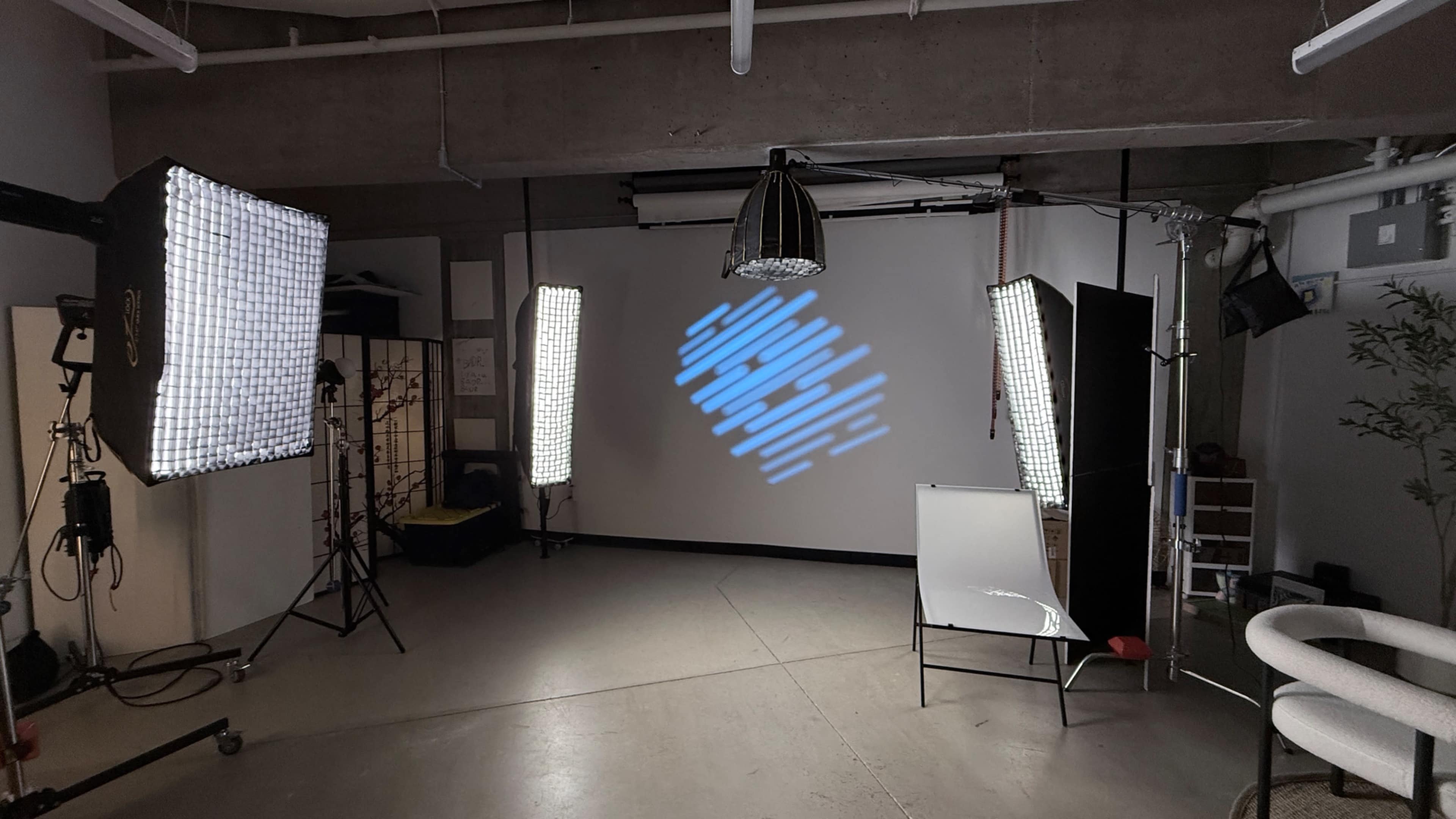 The image shows a photography studio with two lighting setups, a projected backdrop on a screen, and a whiteboard in the foreground.