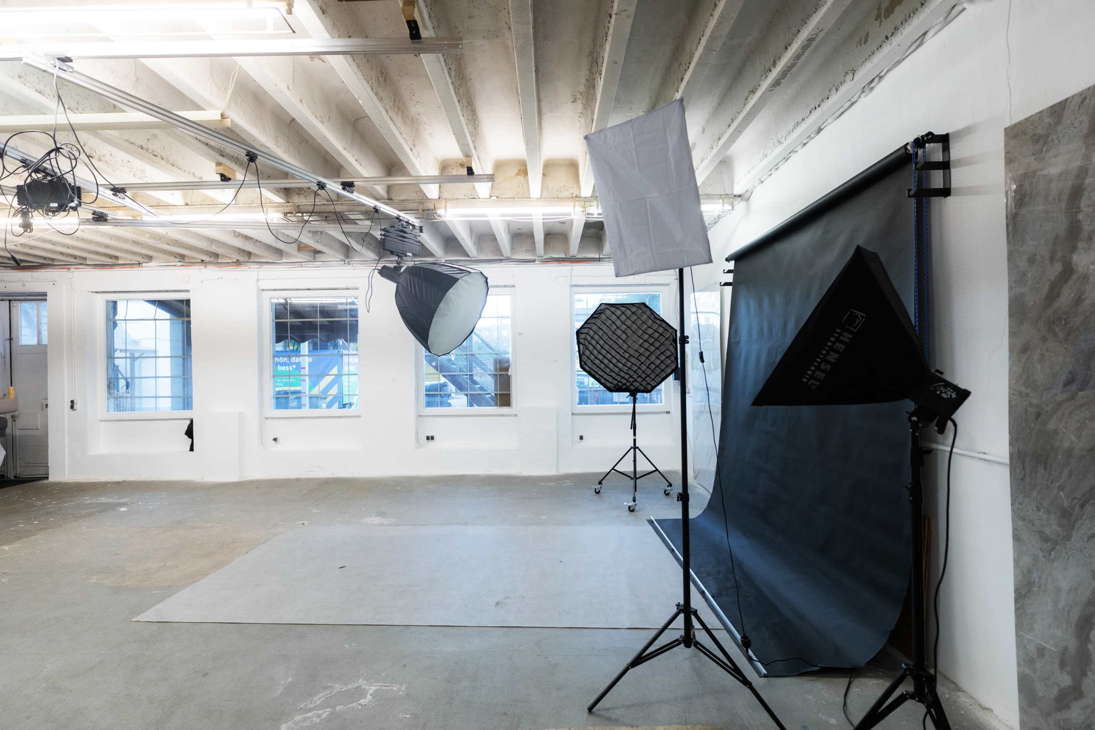 A photography studio features multiple lighting setups and a large backdrop against a plain wall.