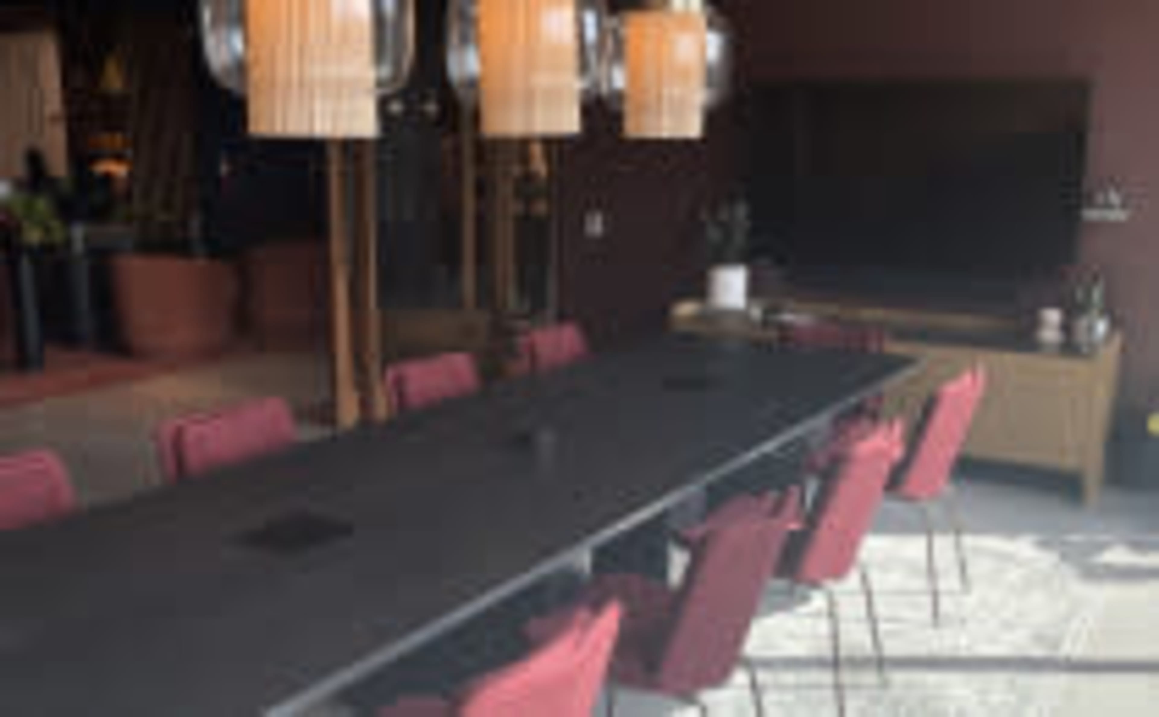A large conference table surrounded by red chairs is positioned in a modern meeting room with a television and decorative plants in the background.