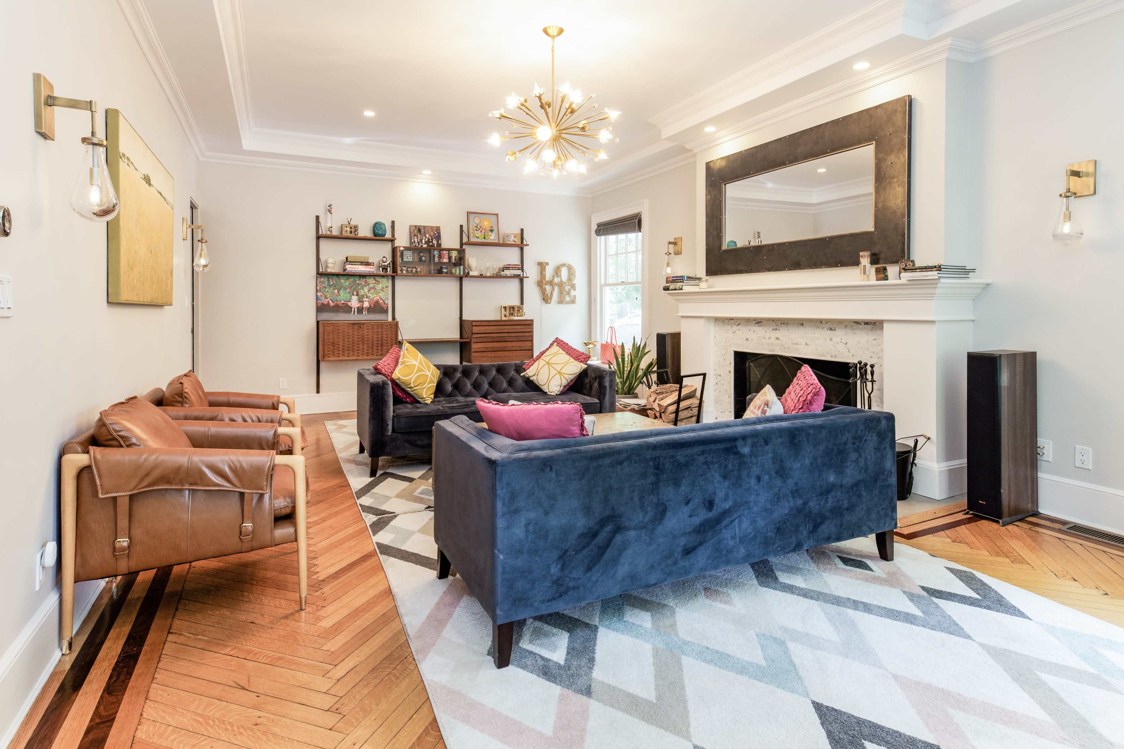 A living room features two couches, armchairs, a coffee table, and a decorative fireplace, all arranged on a geometric patterned rug.