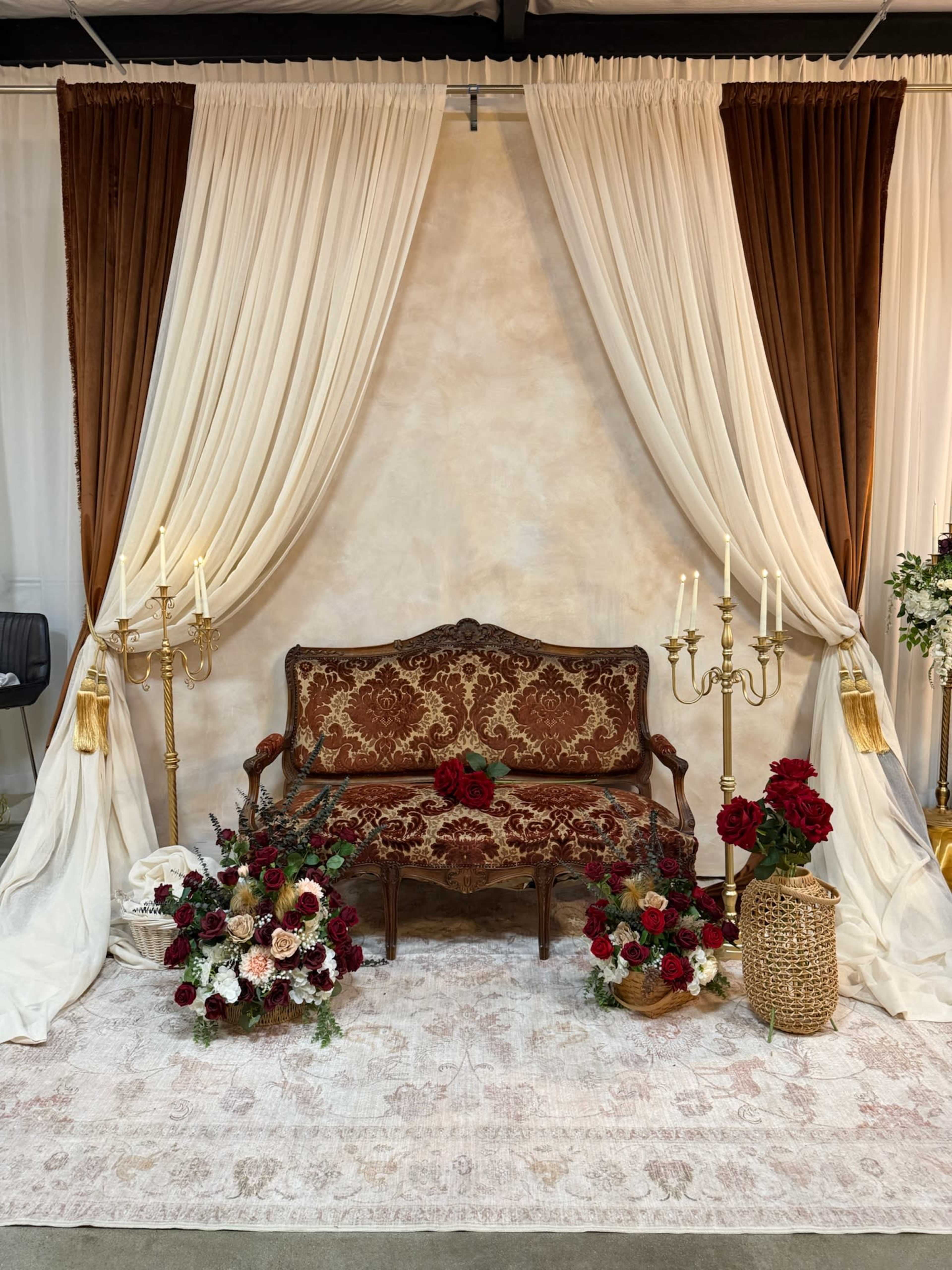 The image features a decorative display with a vintage sofa set against a backdrop of draped fabric, flanked by candelabra and floral arrangements.