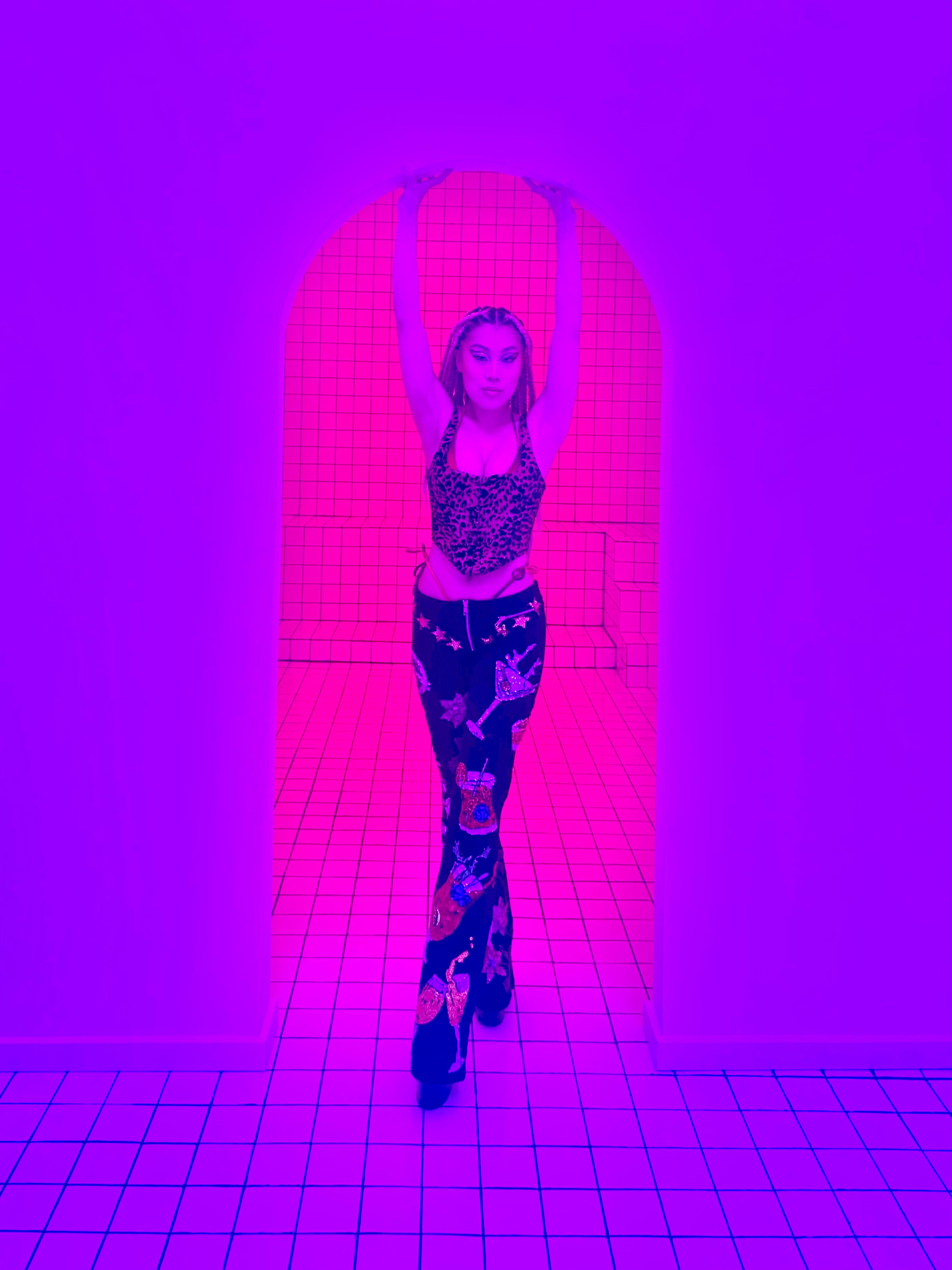 A woman posing for a neon-themed photoshoot in a room with pink and purple lights.