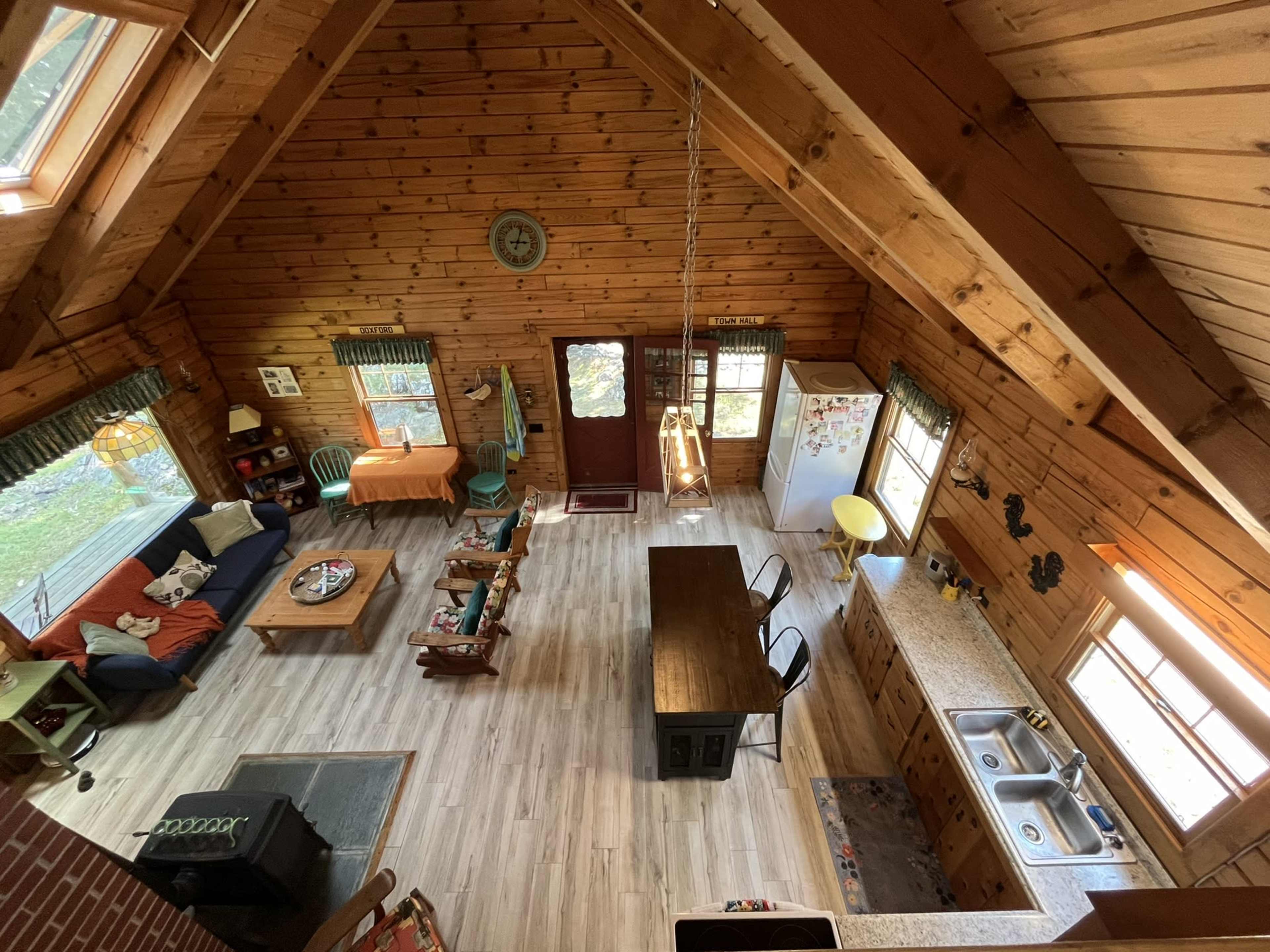 A wooden cabin interior featuring a living area with a couch and coffee table, a dining table, and a kitchen with wooden cabinets and appliances.