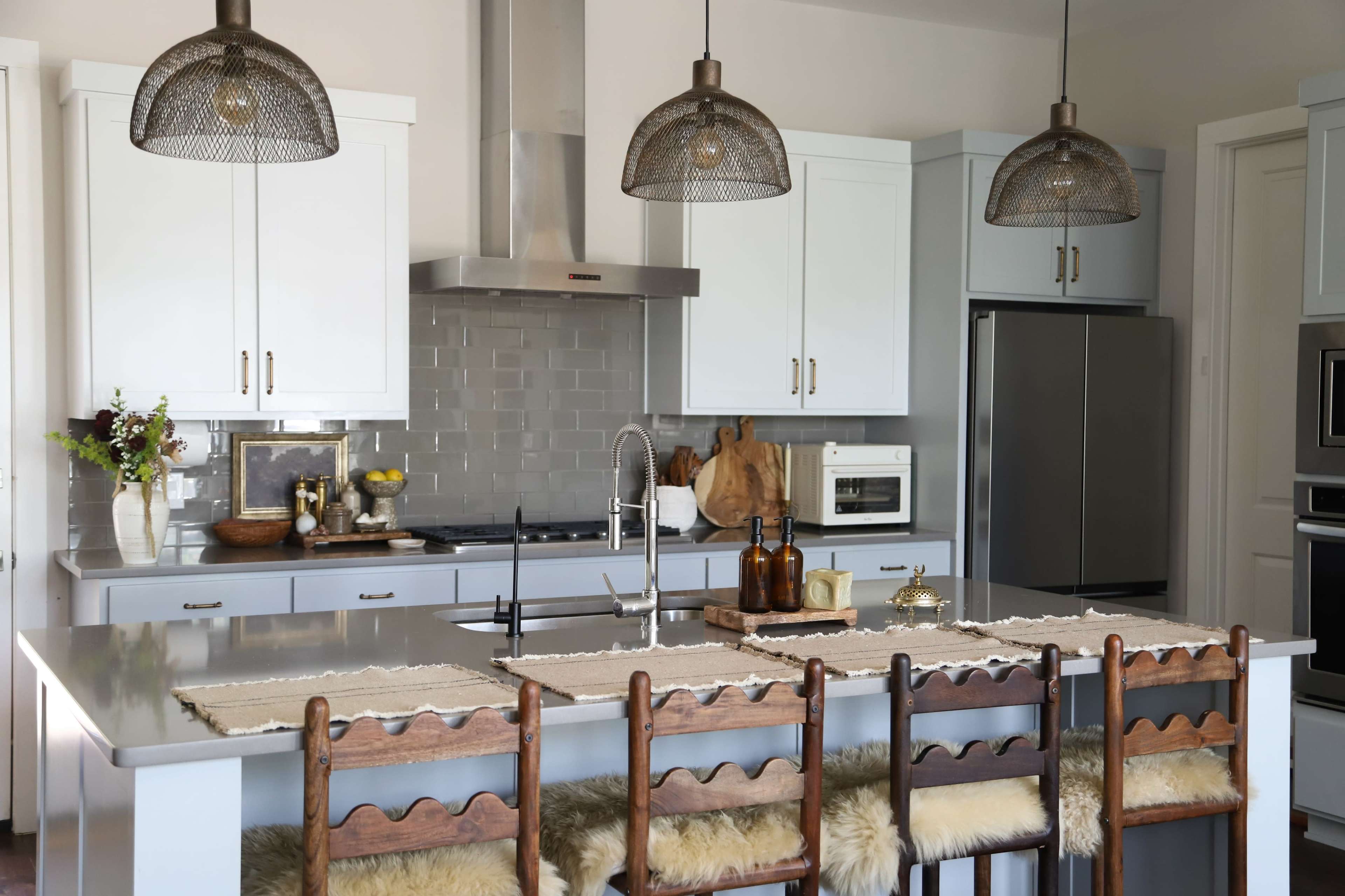 The kitchen features a large island with wooden stools, stainless steel appliances, and modern pendant lighting.